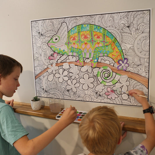 Two children coloring a detailed lizard illustration on a large sheet of paper.