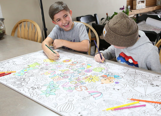 Two children coloring on a large sheet of paper with markers at a dining table.