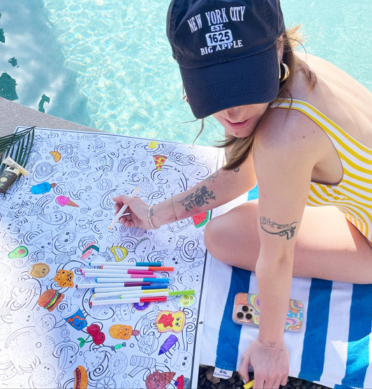 Woman coloring on a beach towel by a pool