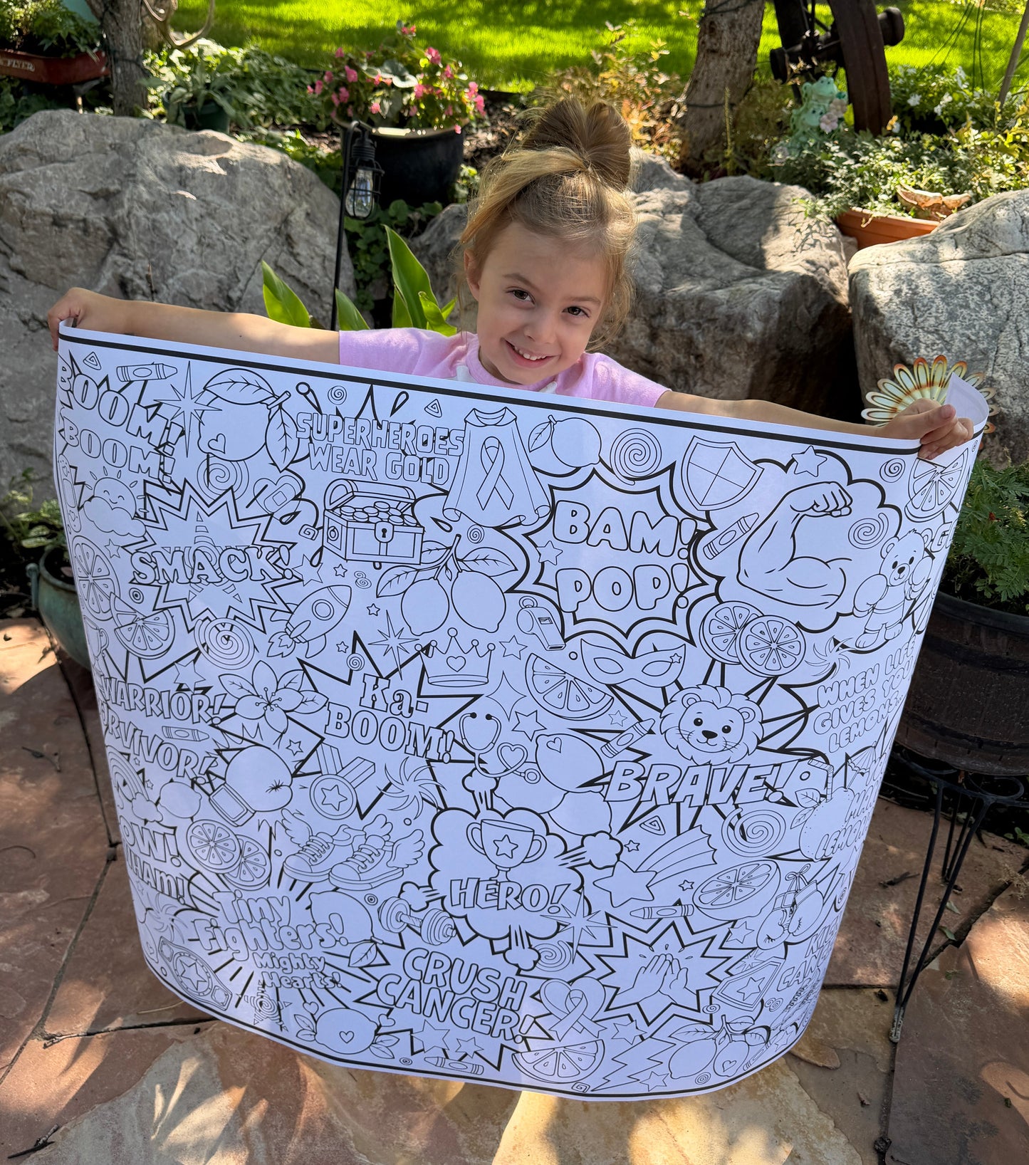 Little girl holding a large coloring poster with childhood cancer ribbons and graphics on it such as a bear with boxing gloves, a lion, lots of lemons, and comic book bursts.