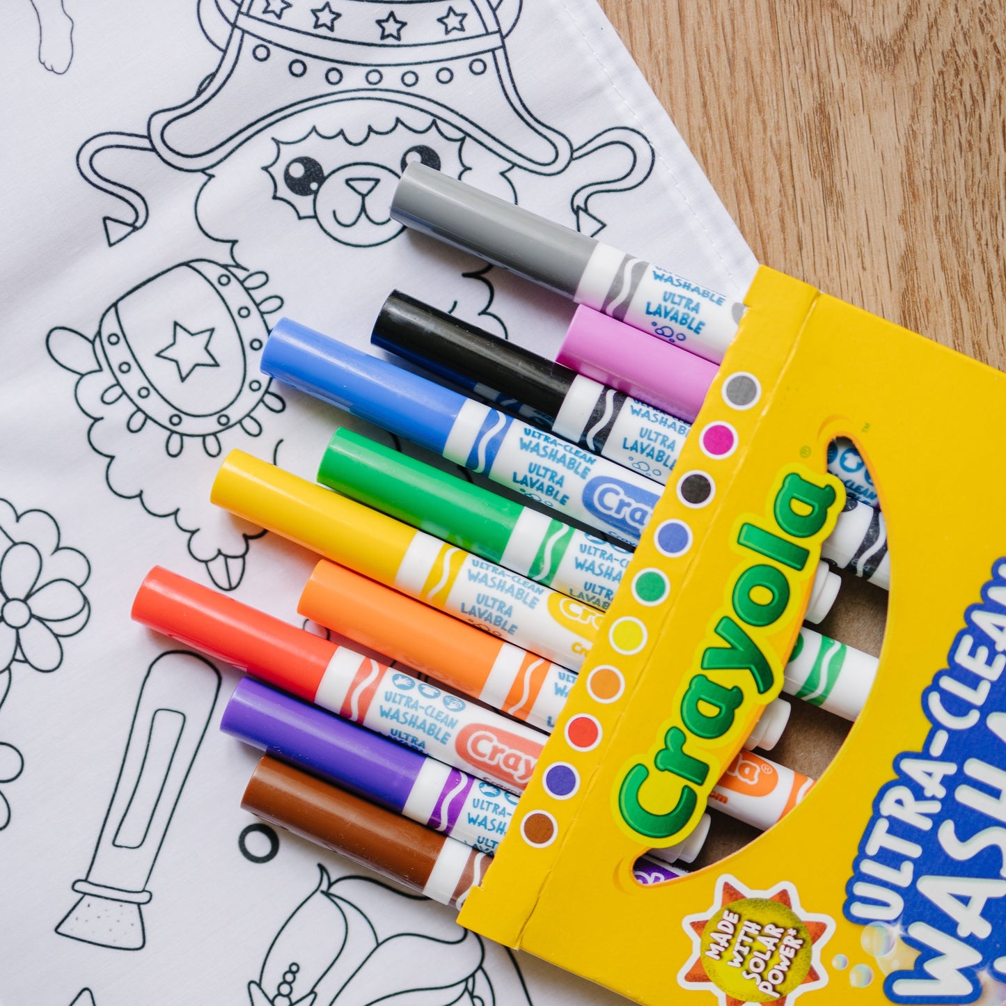 Open box of Markers laid next to an Artistic Chaos Ink fabric coloring tablecloth.