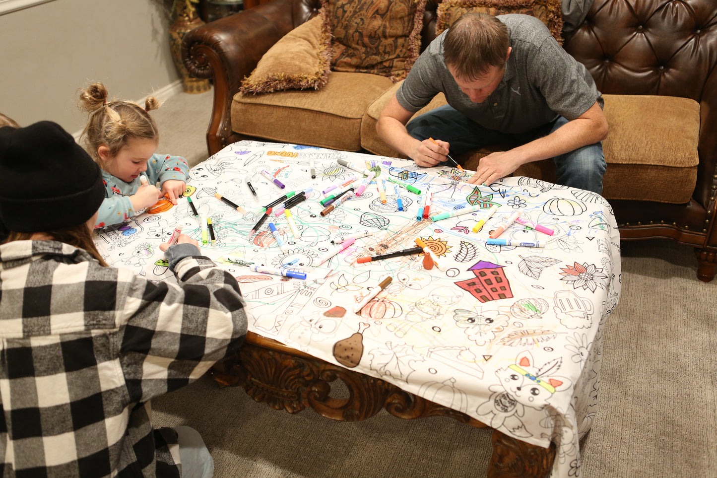 Three people sitting around a table with coloring tablecloth and markers, engaged in a creative activity.