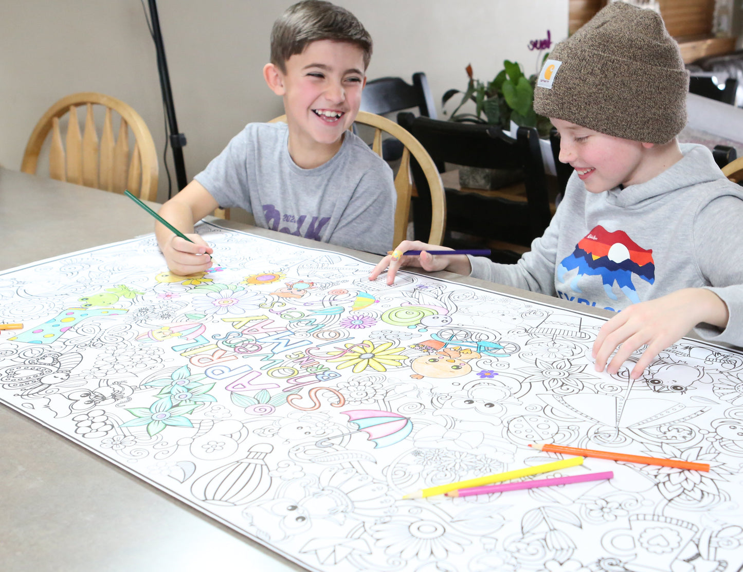 Two children coloring a large sheet of paper with markers at a table.