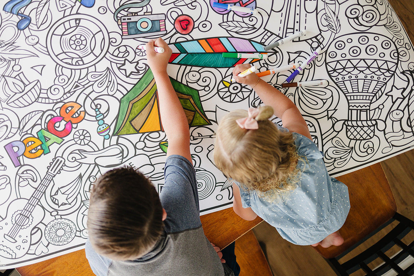 Two children coloring on a large coloring mat with crayons.