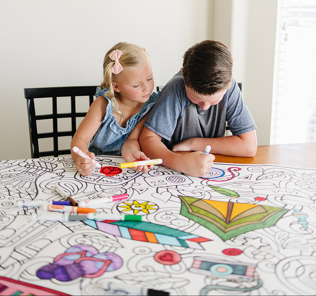 Two children coloring on a large sheet of paper with colorful markers at a table.