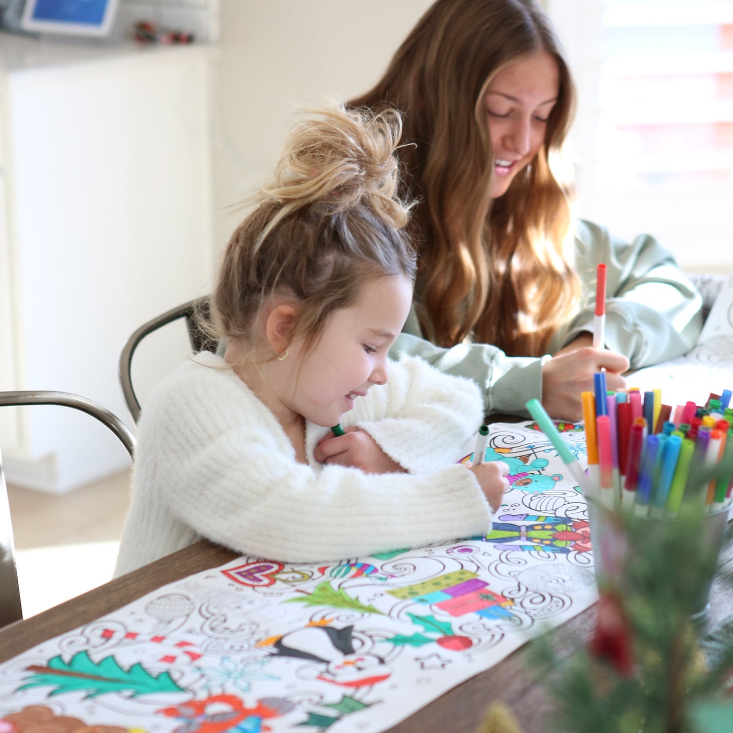 two girls coloring a christmas coloring sheet with nutcrackers, gifts, penguins, etc