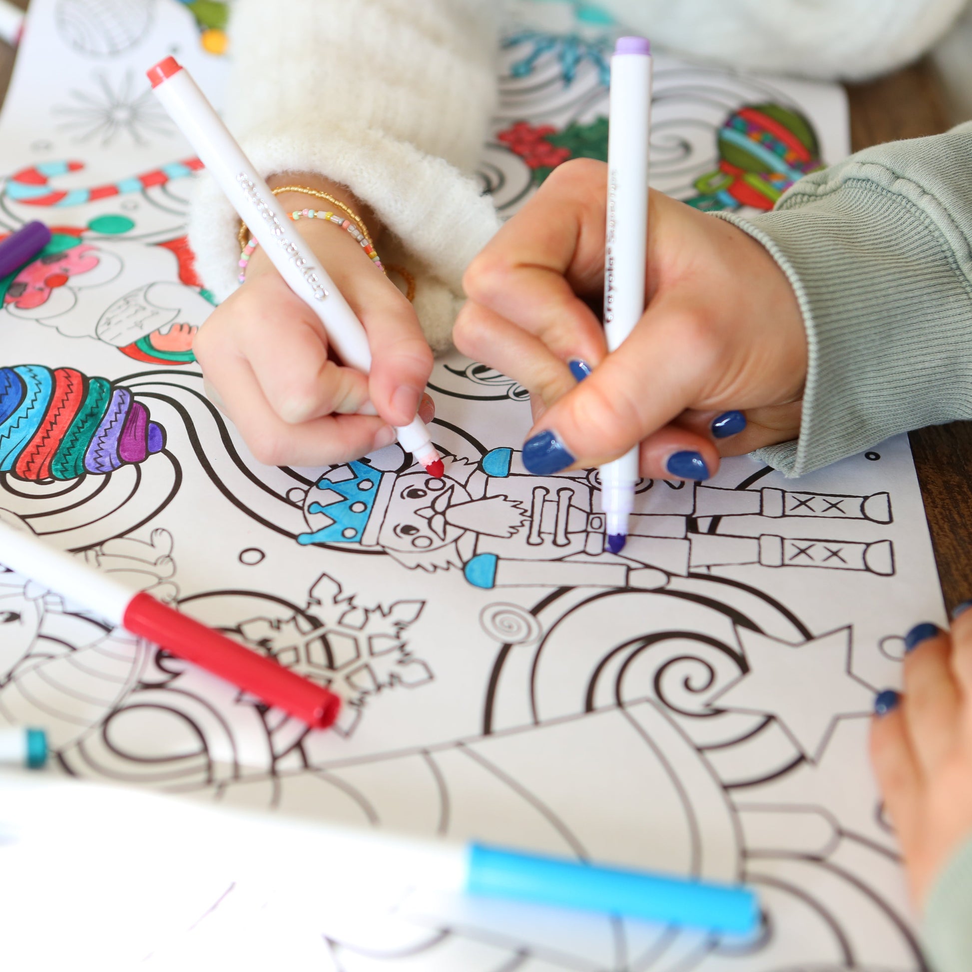Christmas Nutcracker being colored by a childs hand and a bigger hand with blue nail polish