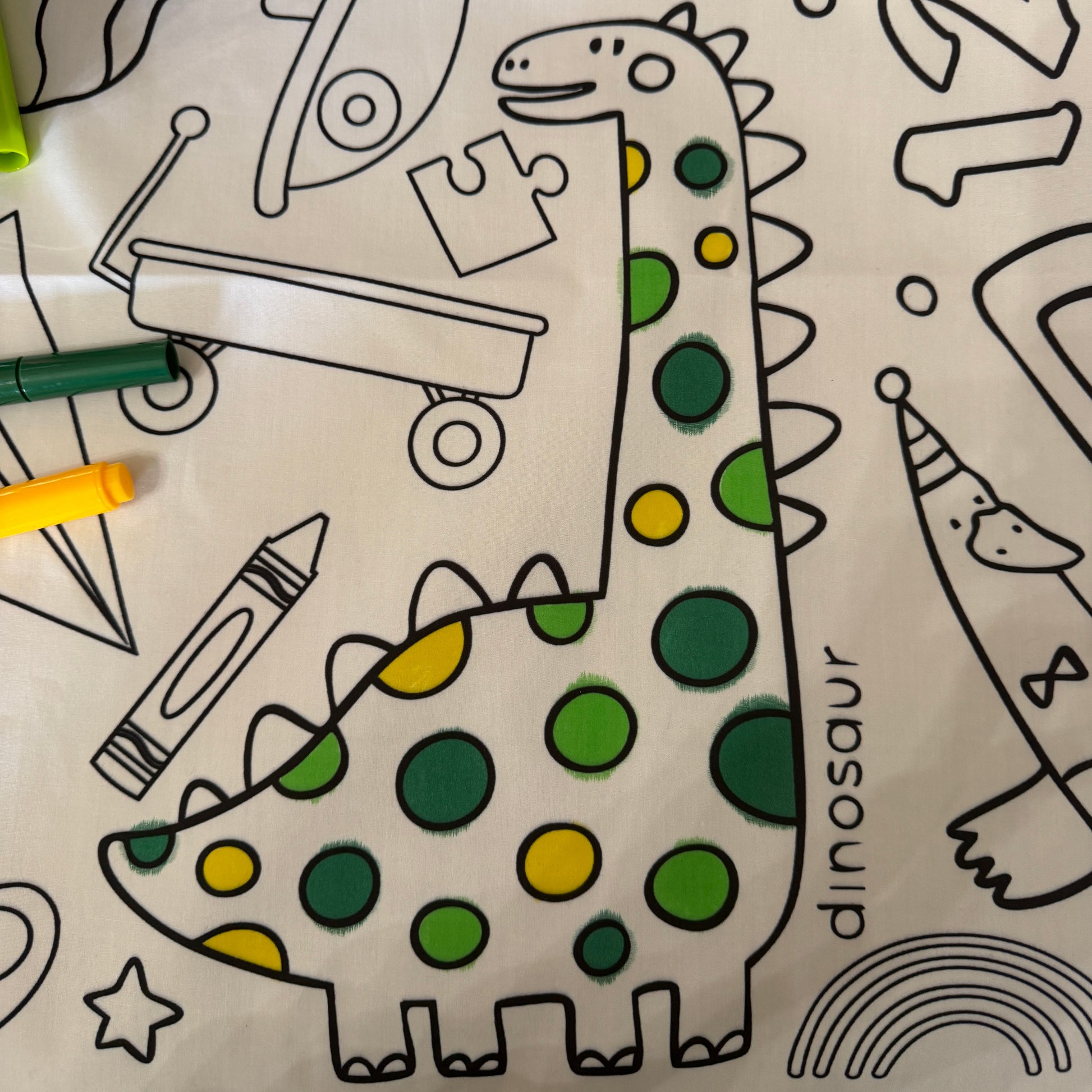 Coloring tablecloth with dinosaur design and coloring tools on a white background
