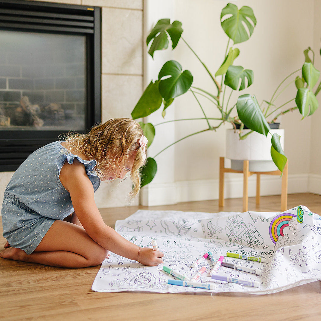 Child coloring on a fantasy coloring mat from Artistic Chaos Ink with washable markers in a cozy living room.