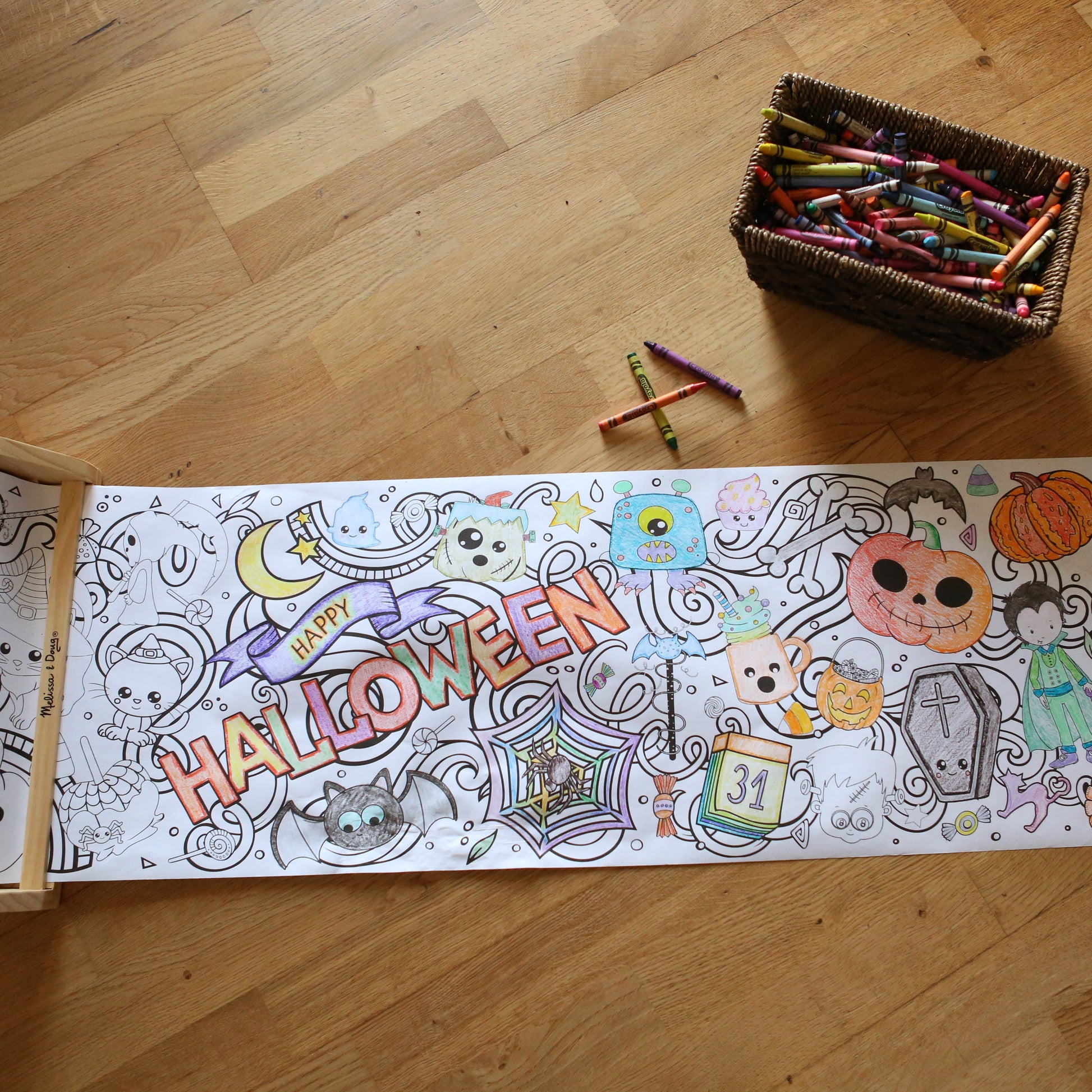 Long Coloring sheet with Halloween-themed illustrations on a wooden floor with crayons.