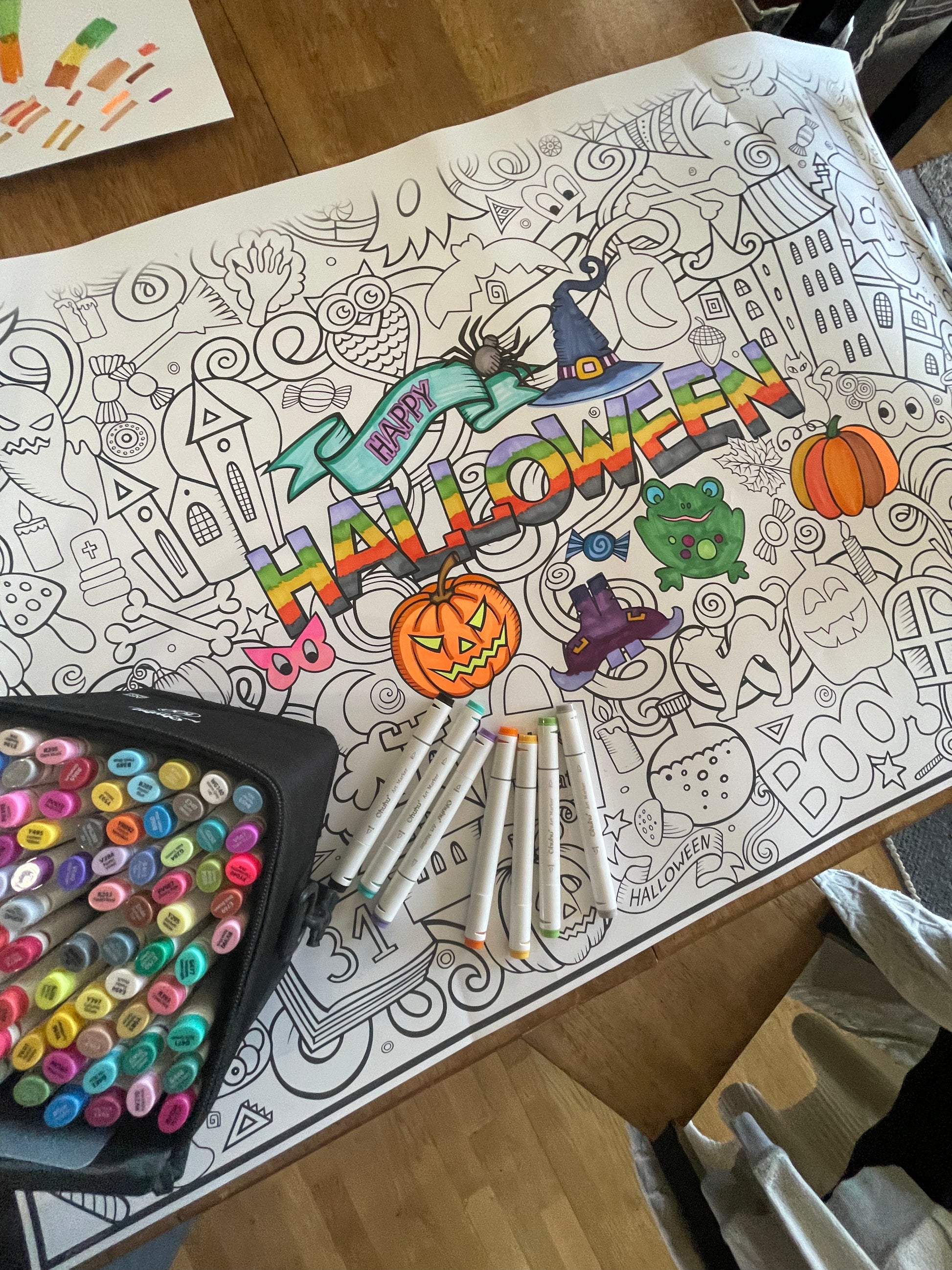 Coloring book with Halloween-themed illustrations and markers on a table