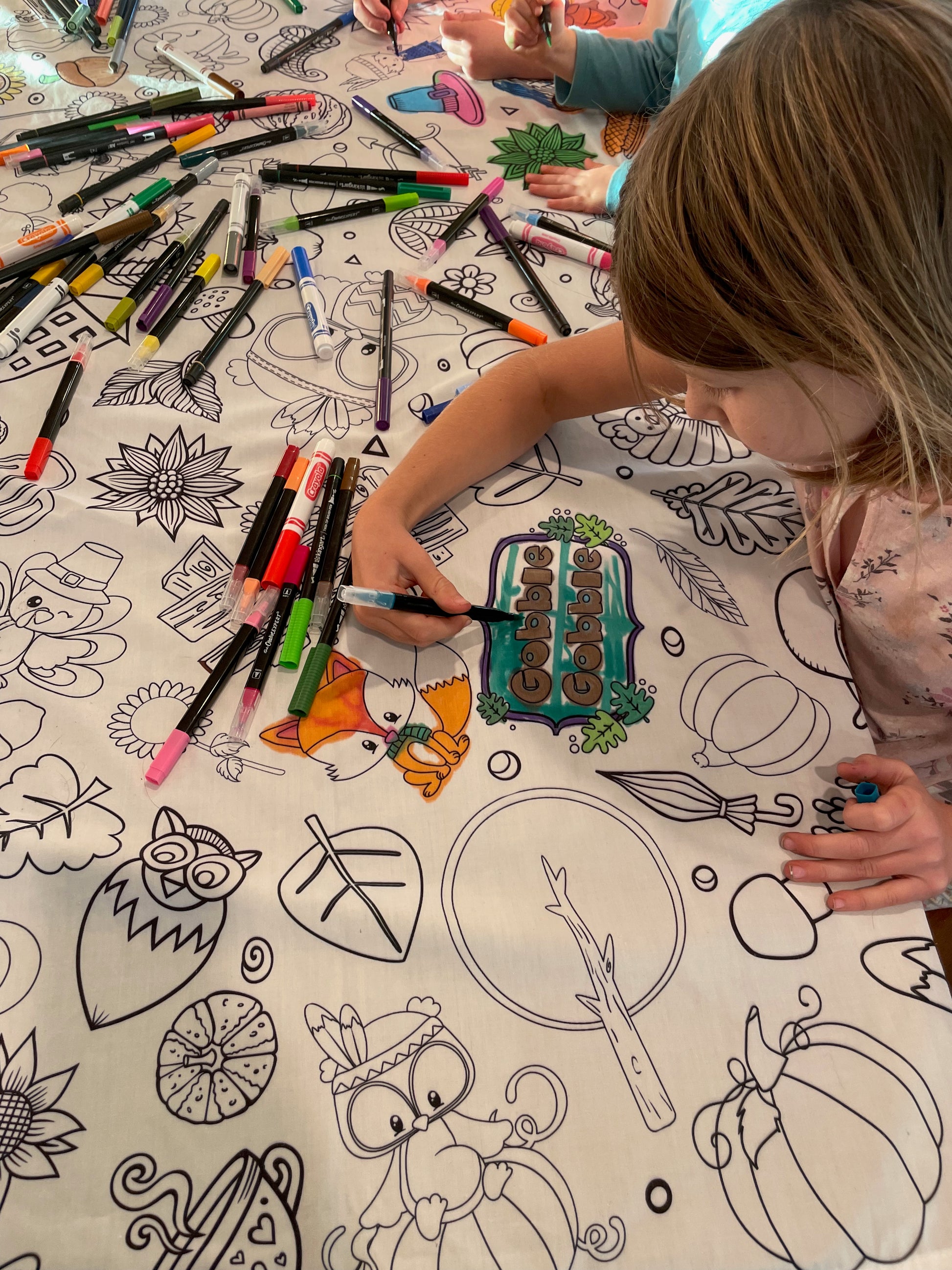 Children coloring on a large sheet with markers and coloring books.