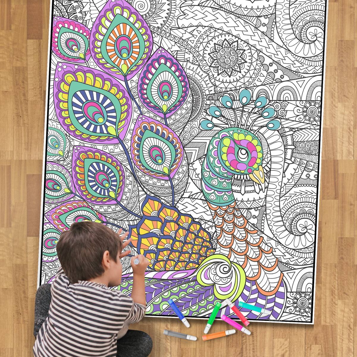little boy coloring a large peacock coloring poster on a wood floor with markers
