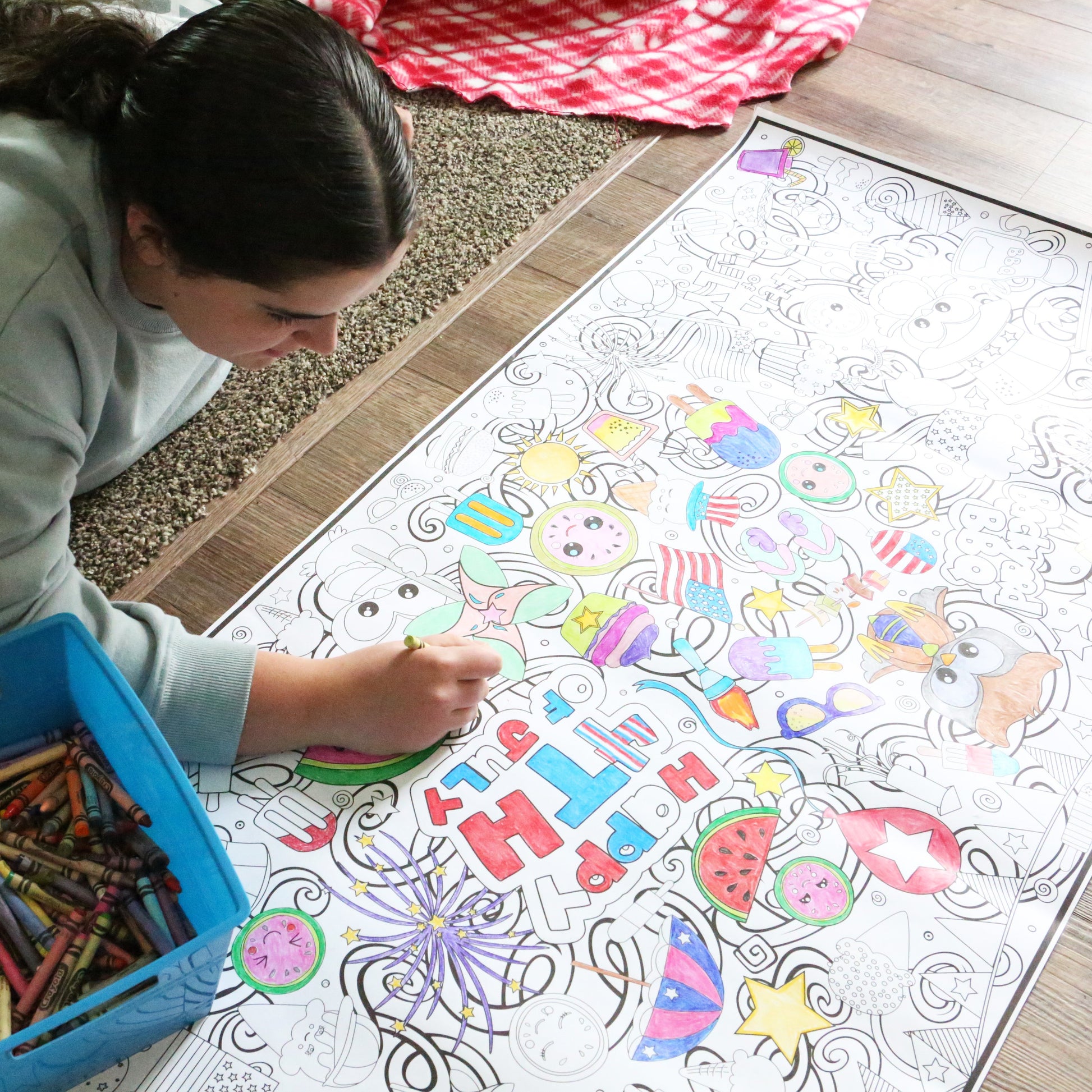 Person coloring on a large mat with crayons on a wooden floor.