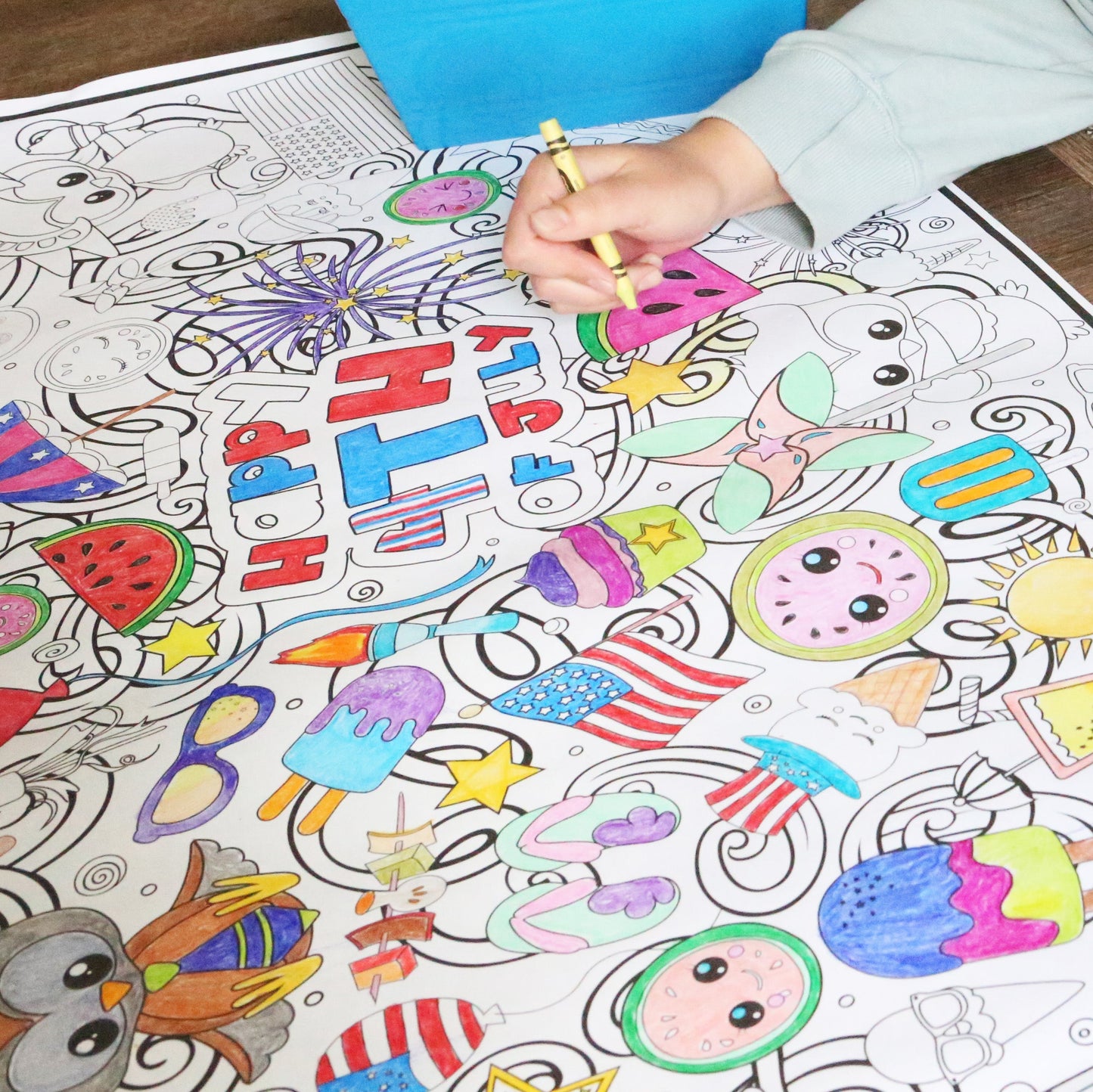 Person coloring a detailed coloring sheet with various illustrations on a wooden table.