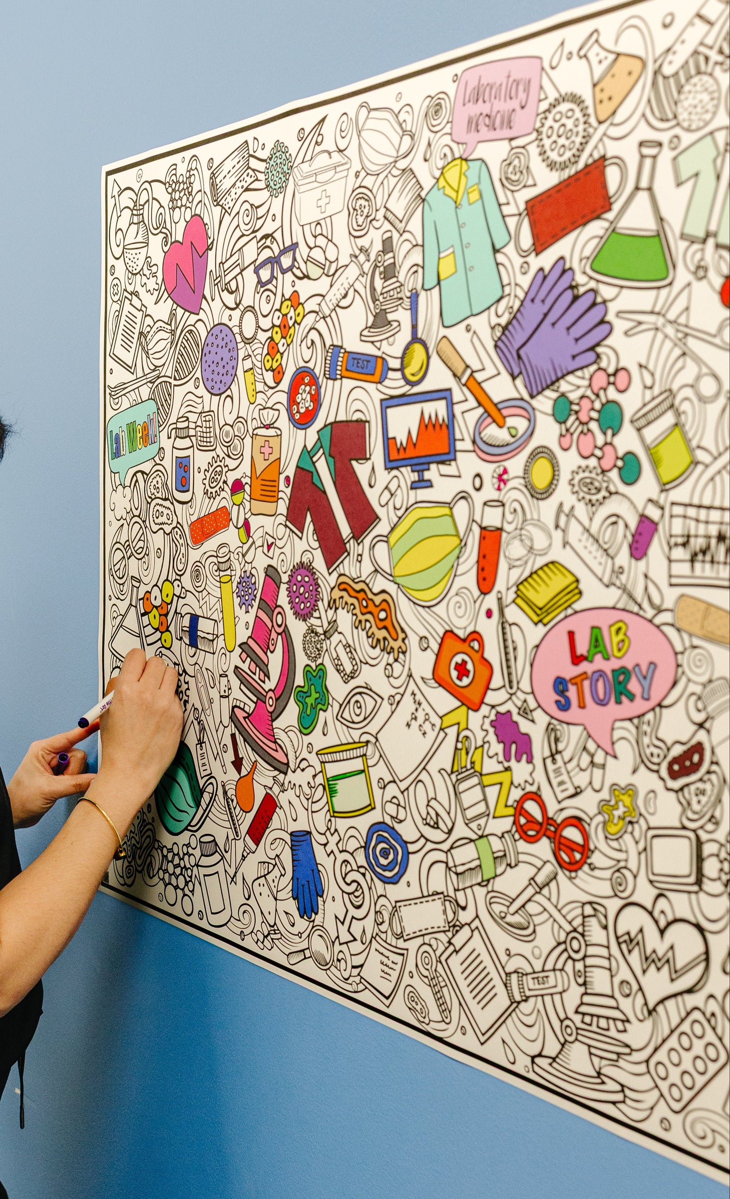 Person coloring a large lab week lab story  art poster on a blue wall