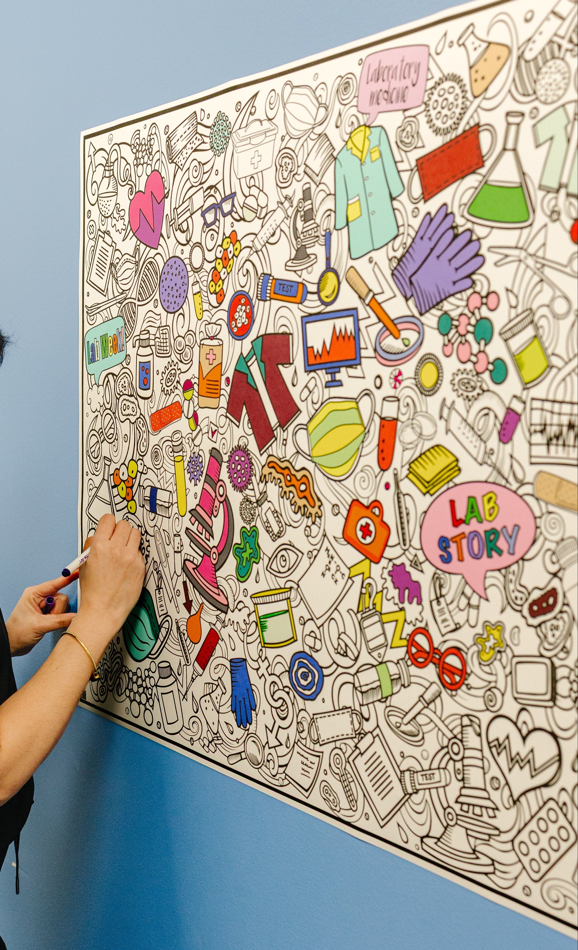 Person coloring a large lab week lab story  art poster on a blue wall