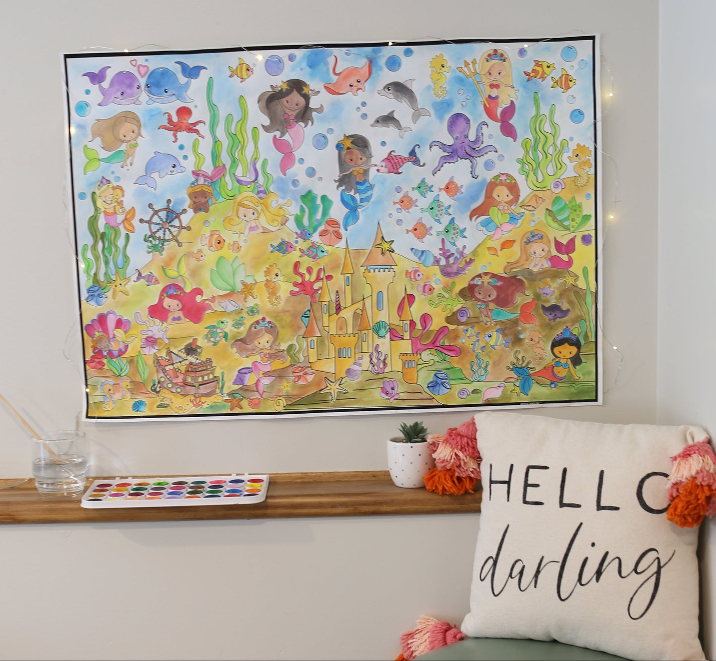 Decorative pillow with 'HELLO' text and green base, next to a colorful mermaid poster on a white wall.