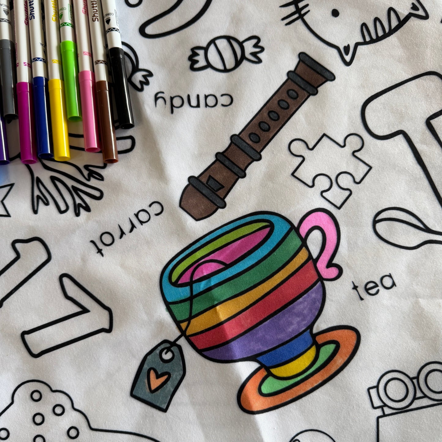 Coloring tablecloth with a rainbow cup, pens, and various illustrations for younger children and markers.