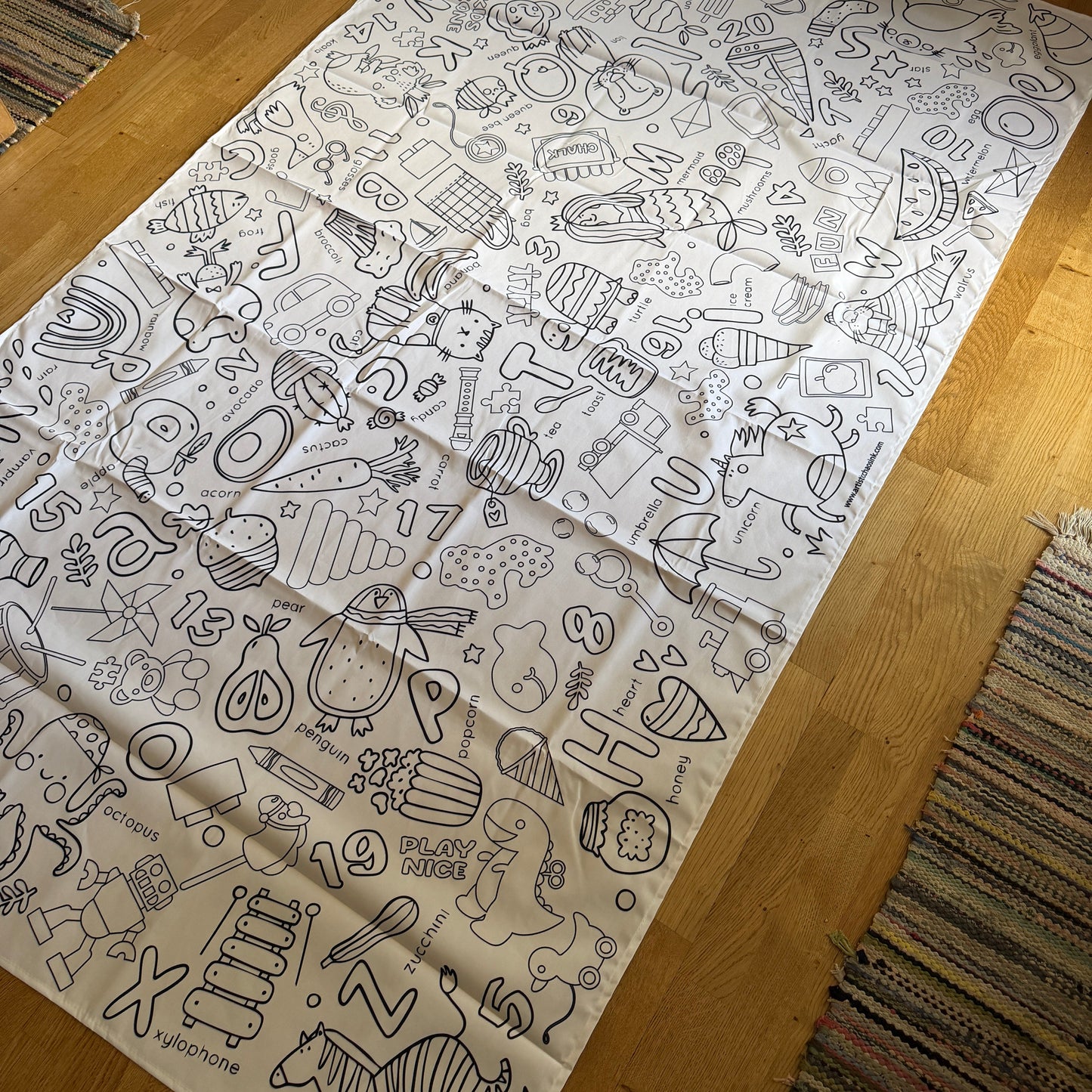 Large fabric coloring tablecloth with various preschool and letter illustrations on a wooden floor.