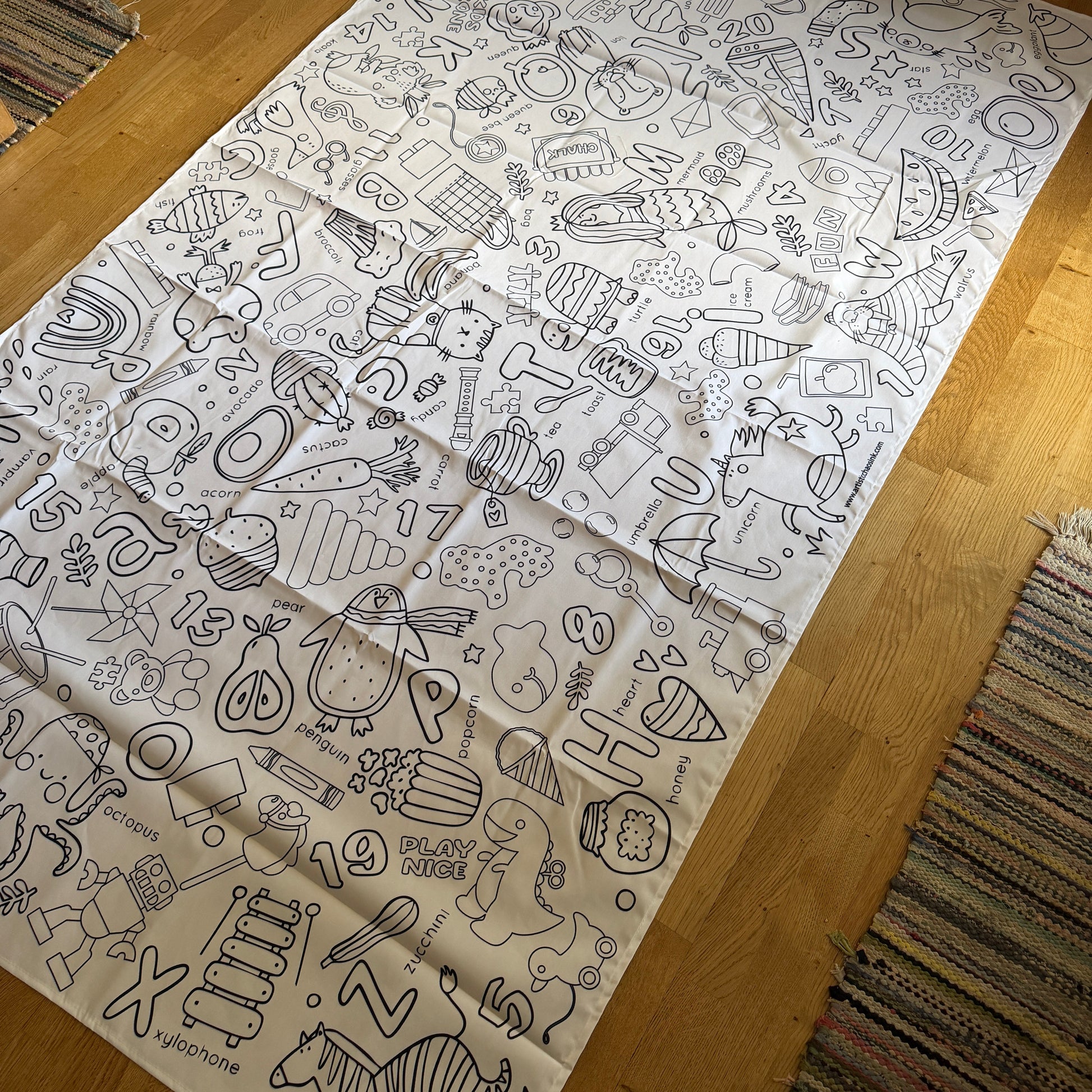Large fabric coloring tablecloth with various preschool and letter illustrations on a wooden floor.
