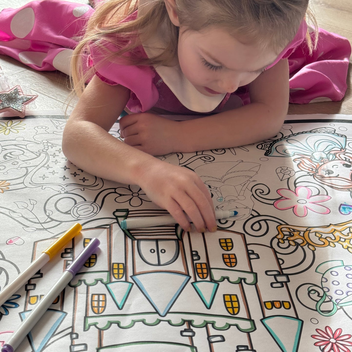 Child coloring a castle on a large coloring book with markers.