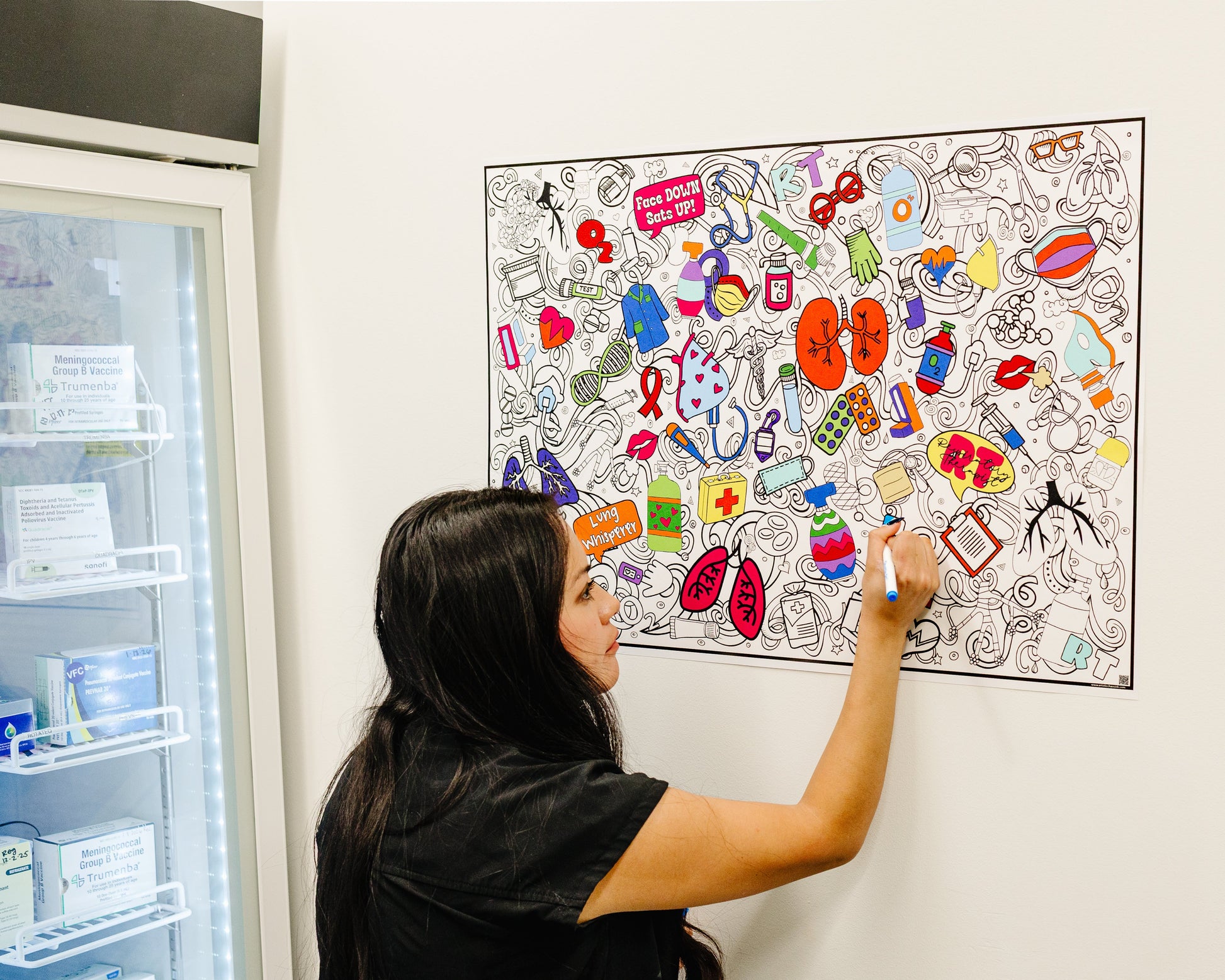medical personnel interacting with a colorful coloring poster on a wall with lungs and breathing equipment.