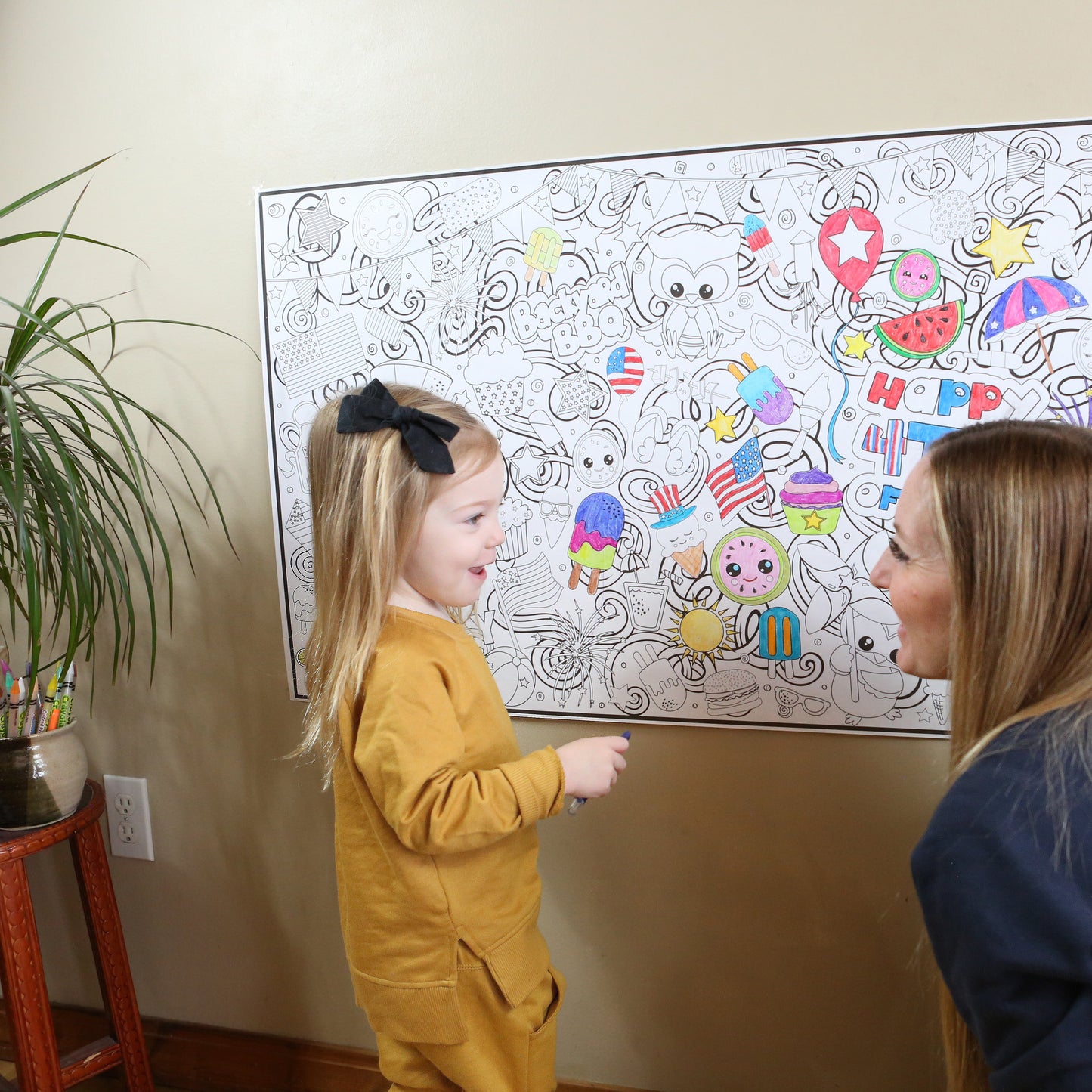 Woman and child looking at a large coloring poster on a wall with 4th of july graphics, popsicles and fruit