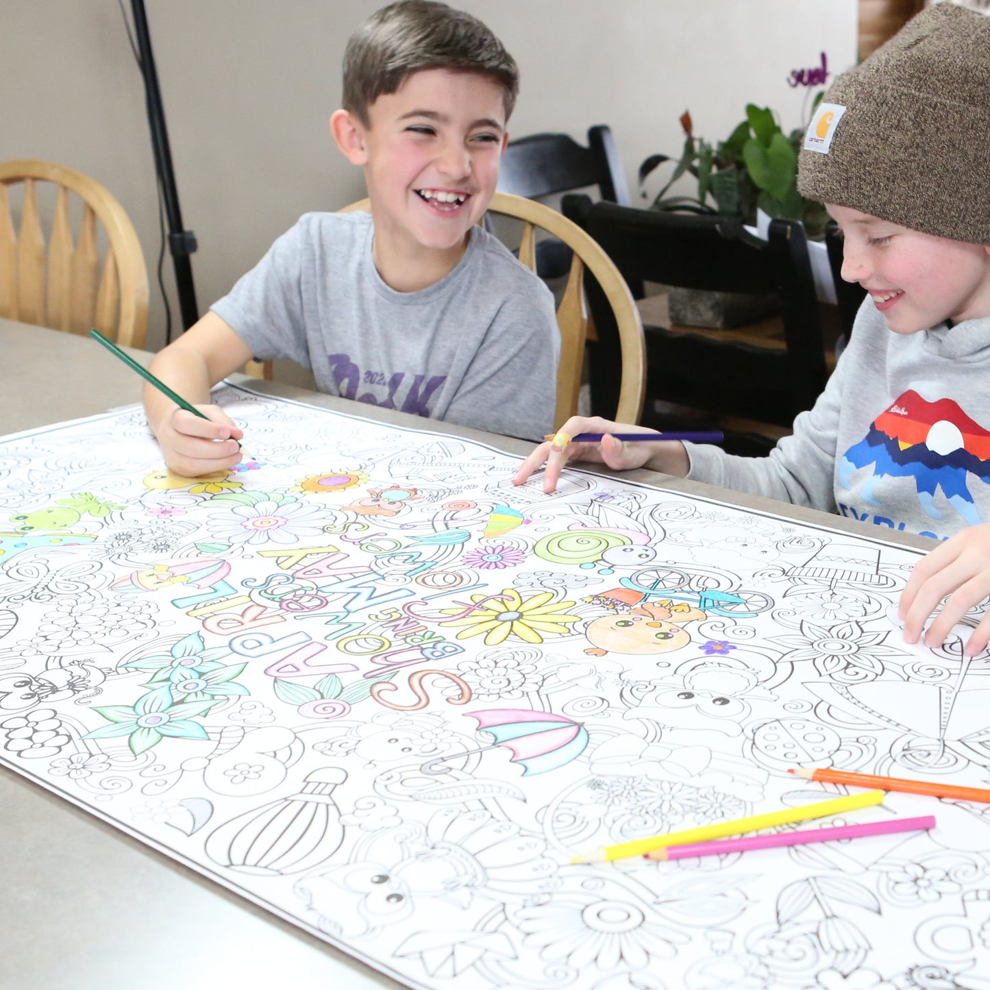 Two children coloring a large spring time coloring sheet of paper designed by Artistic Chaos Ink with markers at a table.