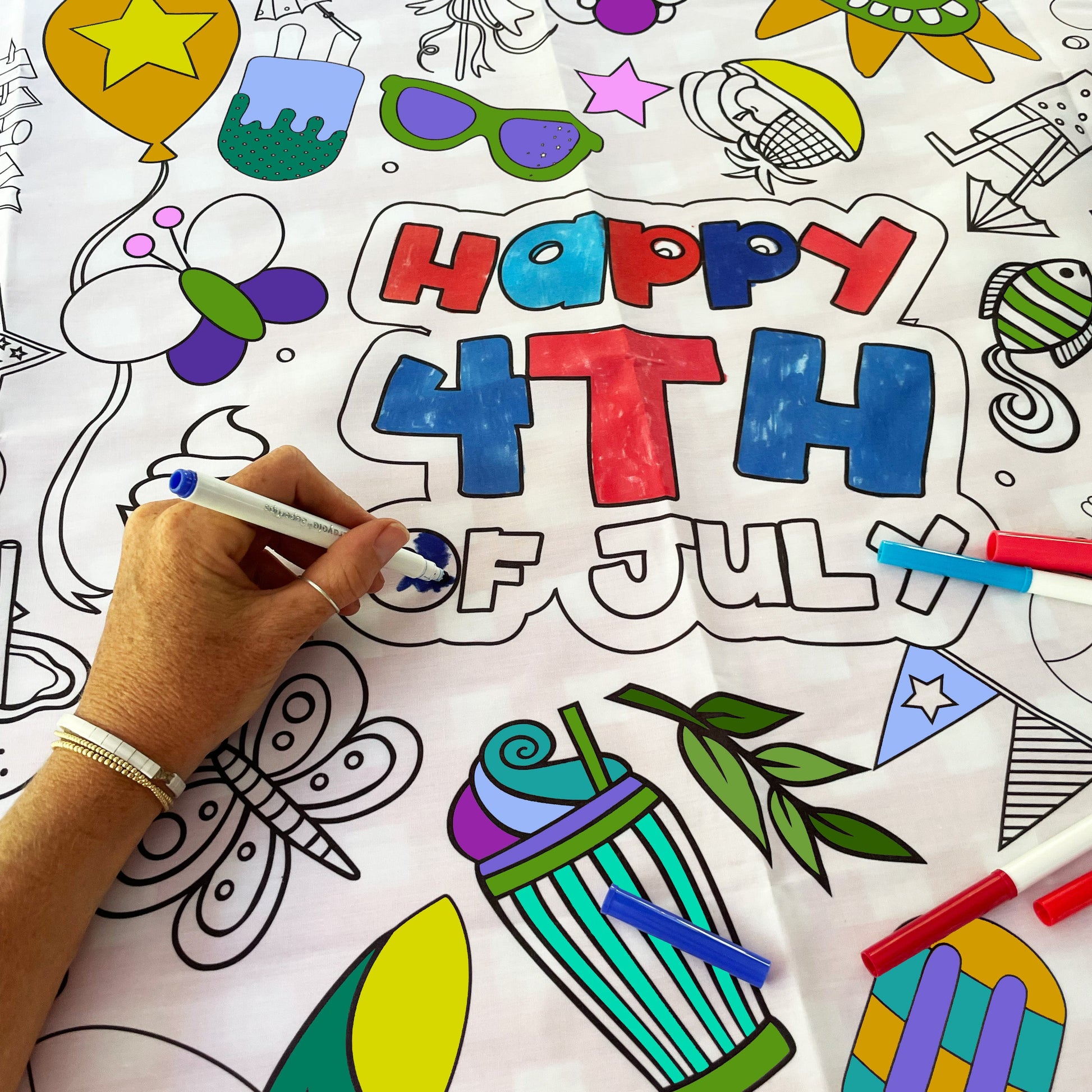 Coloring sheet with 'Happy 4th of July' text and various illustrations, being colored by a hand.