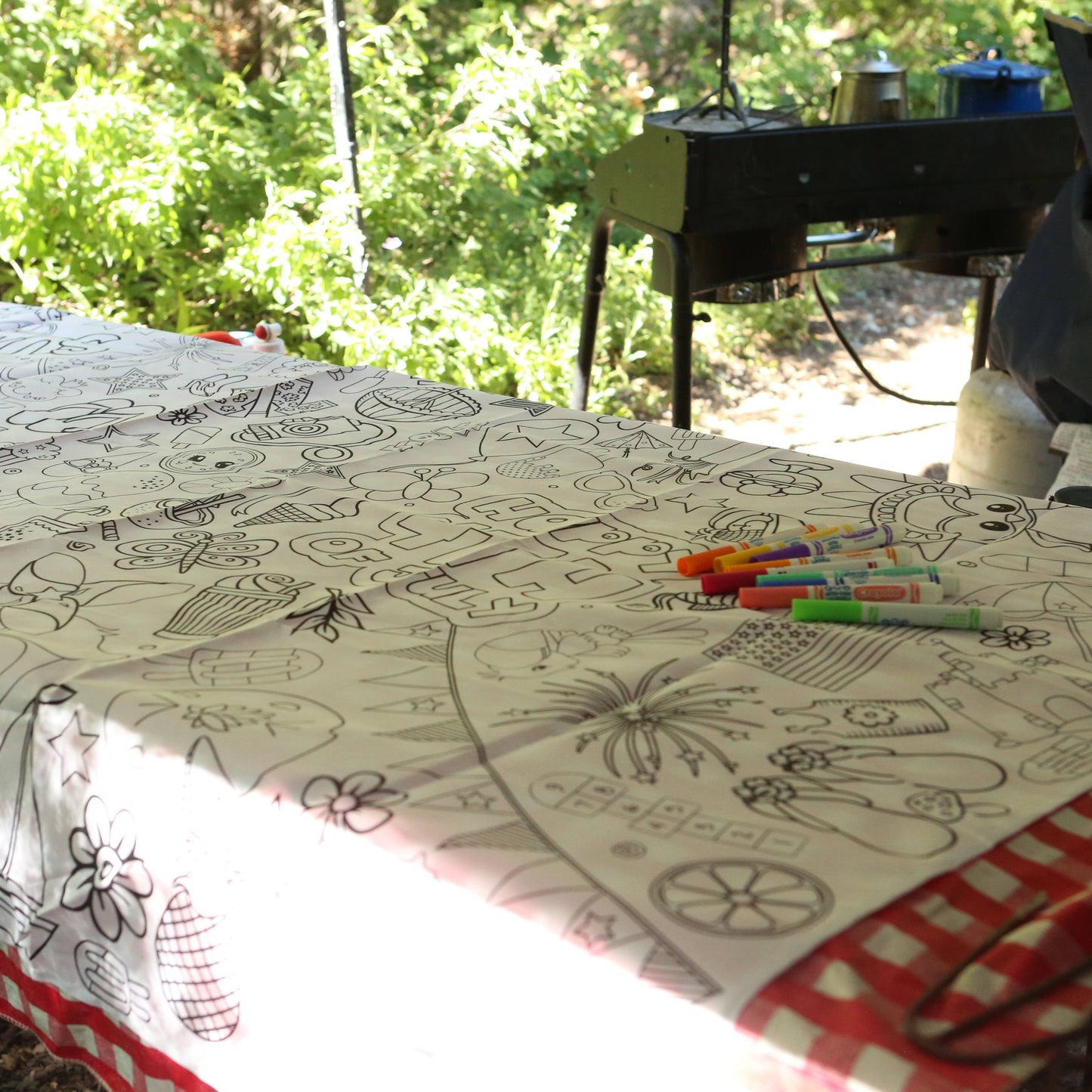 Table with a decorative tablecloth featuring black and white designs, with markers on top, outdoors.