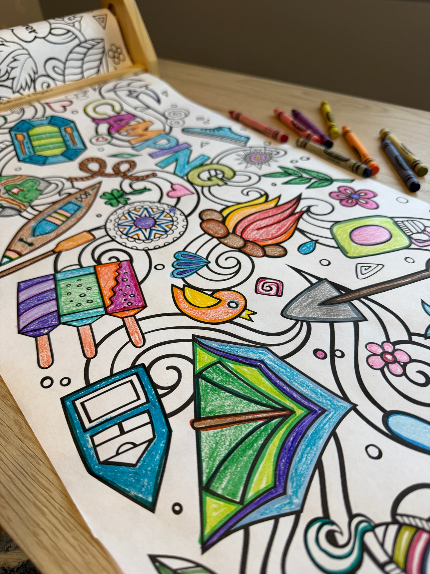 Coloring roll paper with tent, popcicles, camp fire, raft, canoe, shovel, rope and more. Crayons are sitting to the side.  