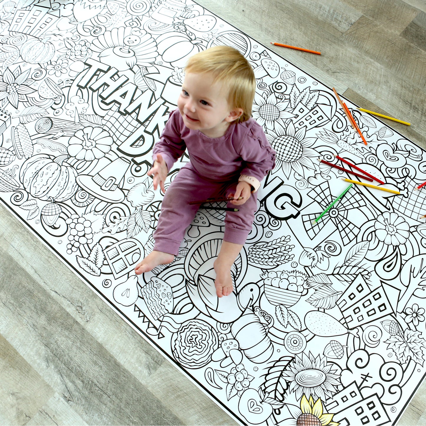 large coloring banner on the floor with small baby sitting on it to show size. Coloring banner has fall and thanksgiving graphics on it. 