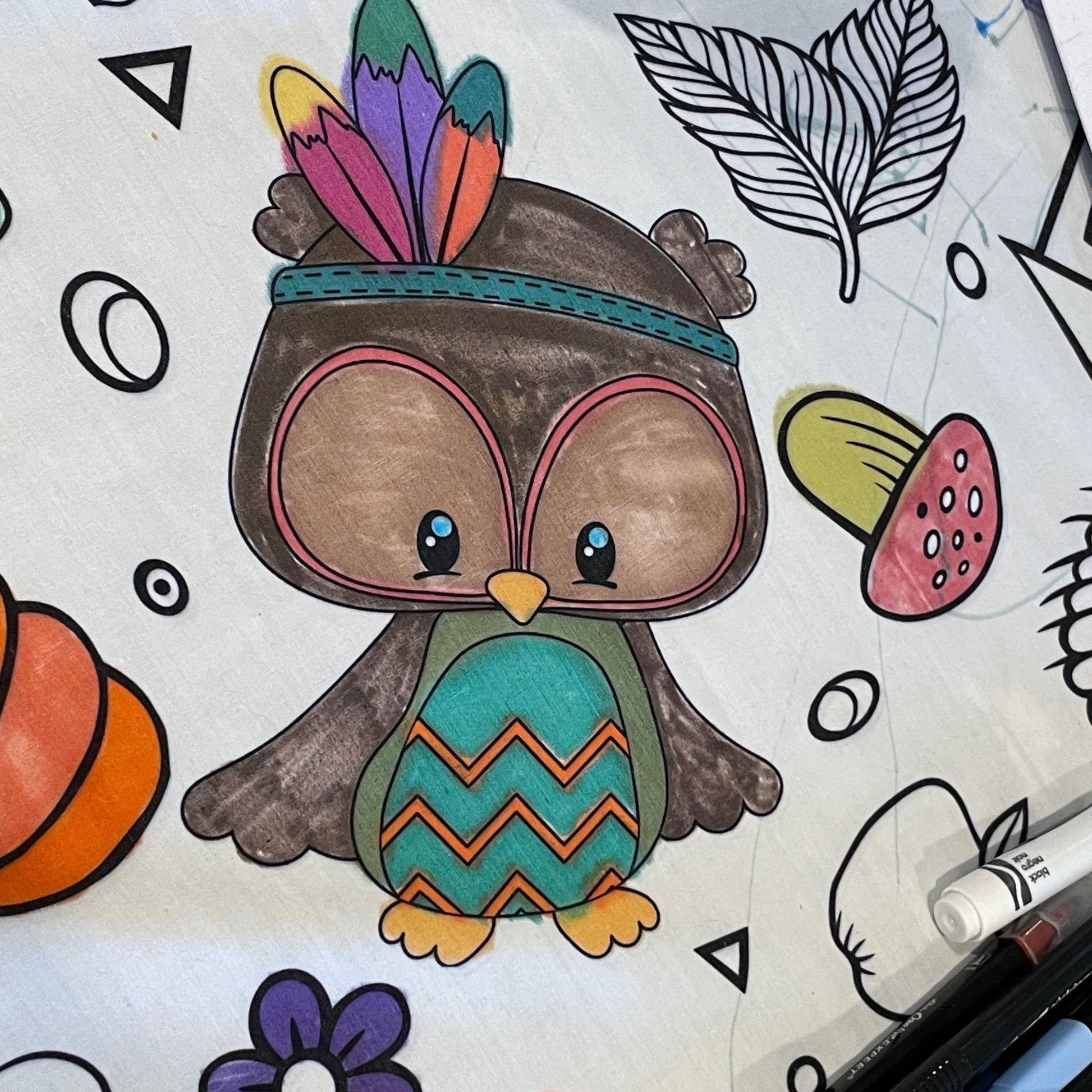 Colorful owl illustration with tribal headdress on a fabric coloring tablecloth with markers.