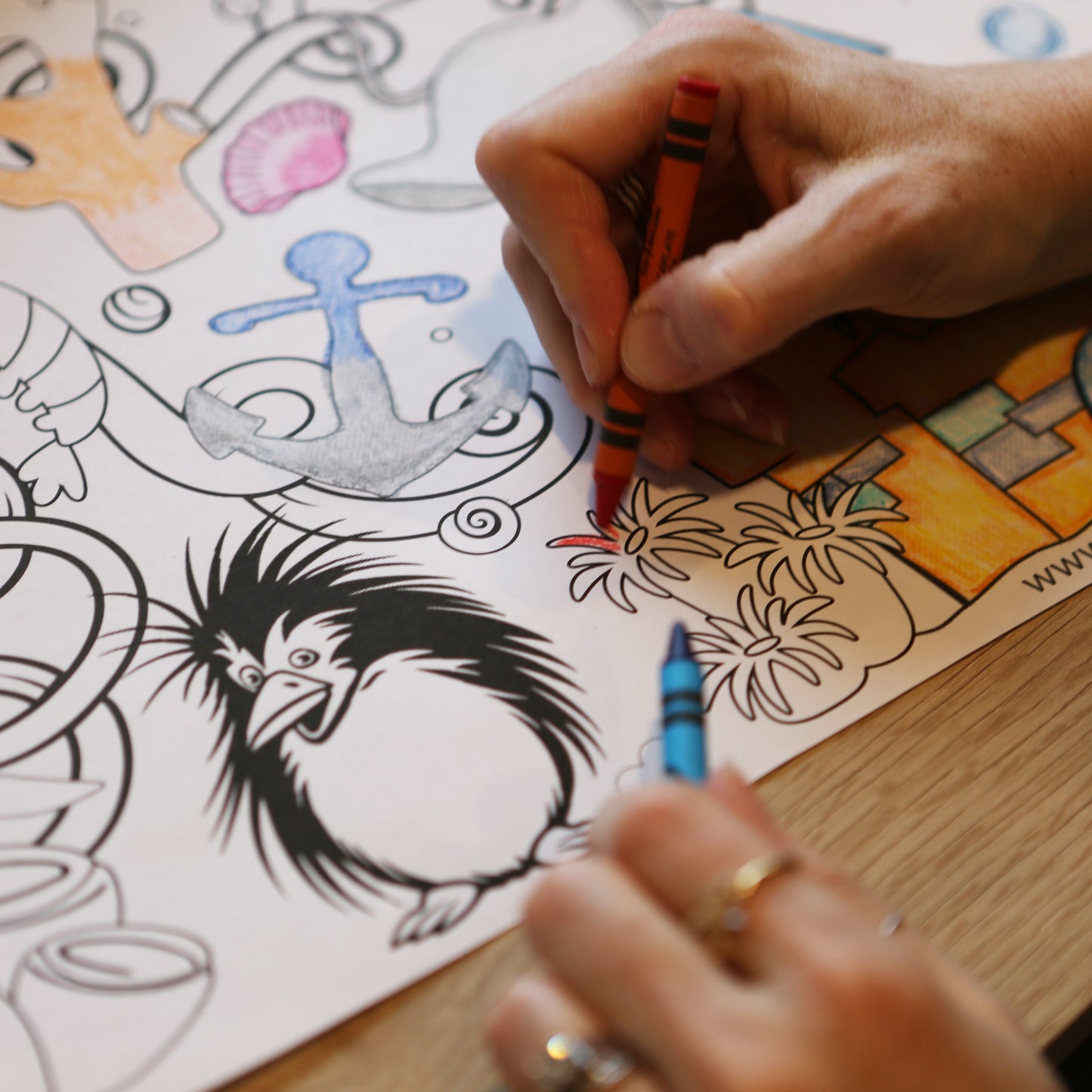 A hand coloring a sea urchin on a large coloring sheet of under water designs