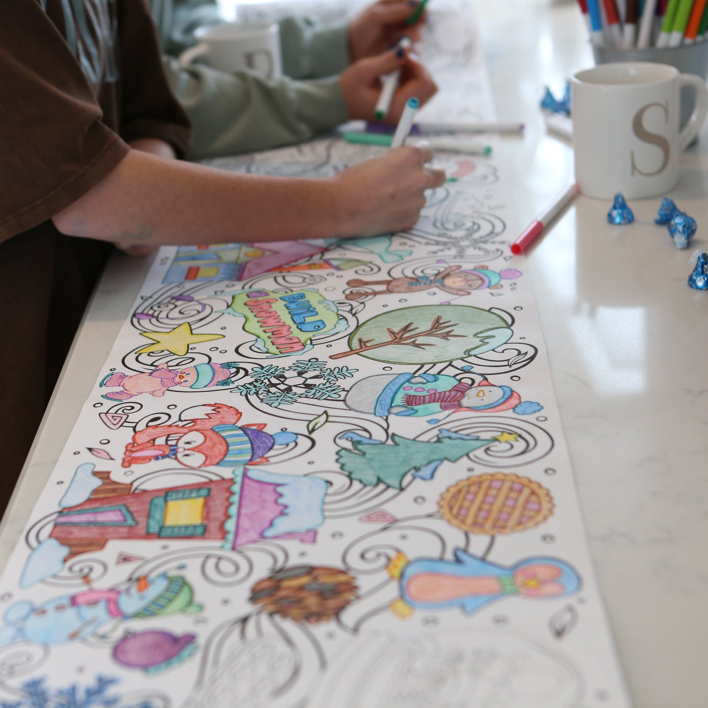 two girls coloring on a winter themed coloring poster. A fox, snowman, trees, pinecone, star, penguin and more.
