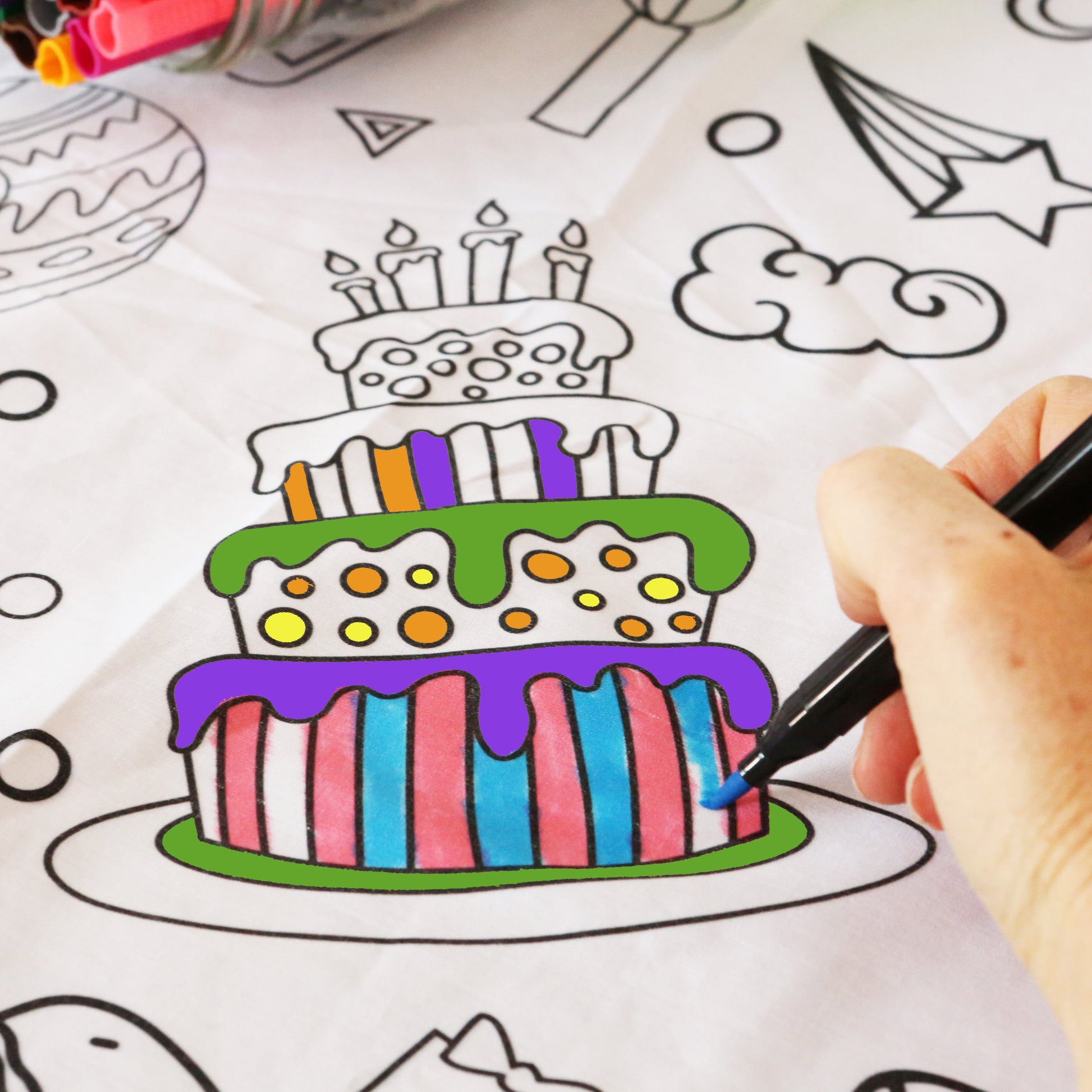 Birthday themed Coloring fabric tablecloth with a cake illustration and a hand coloring it with a washable marker