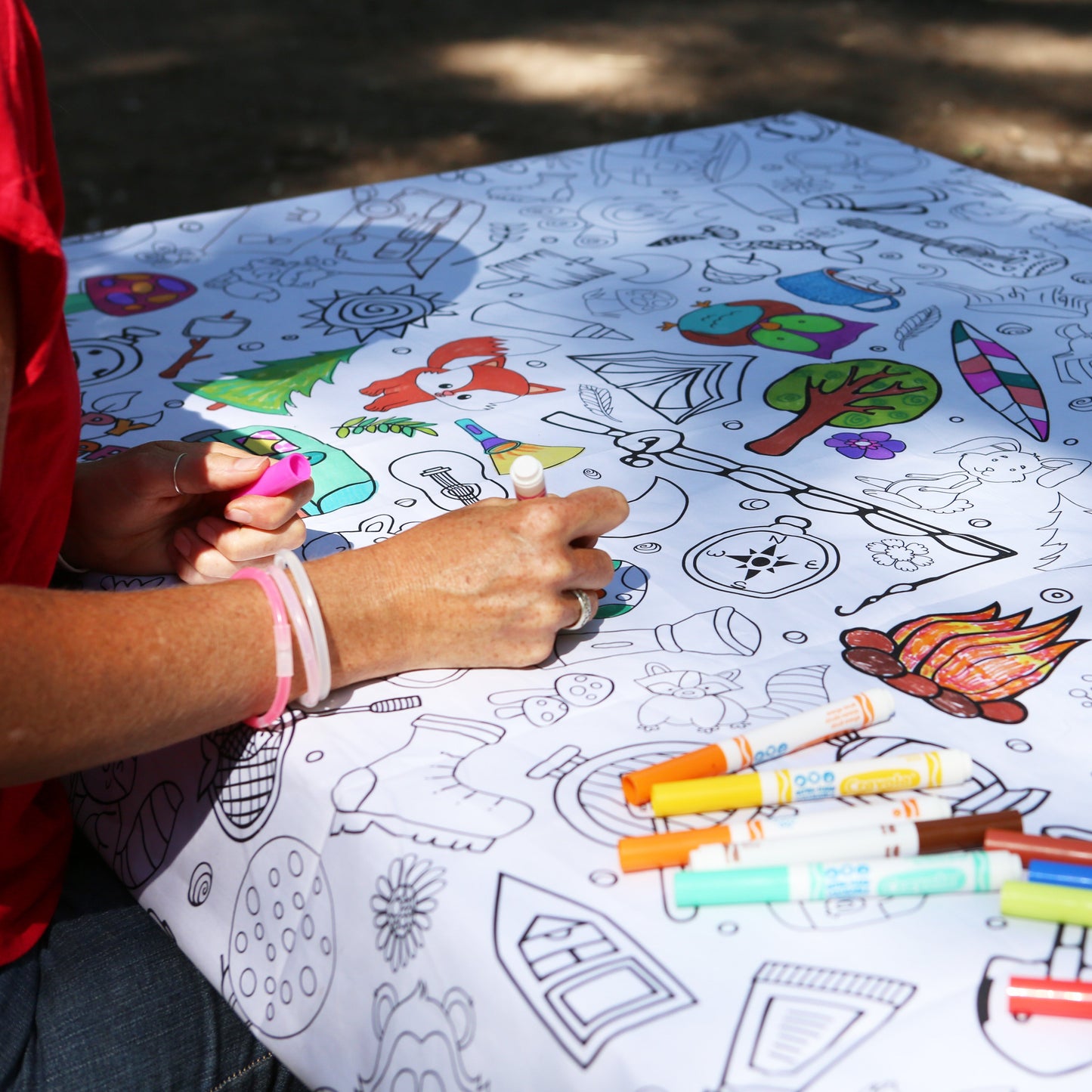 Person coloring on a large fabric coloring tablecloth with markers outdoors