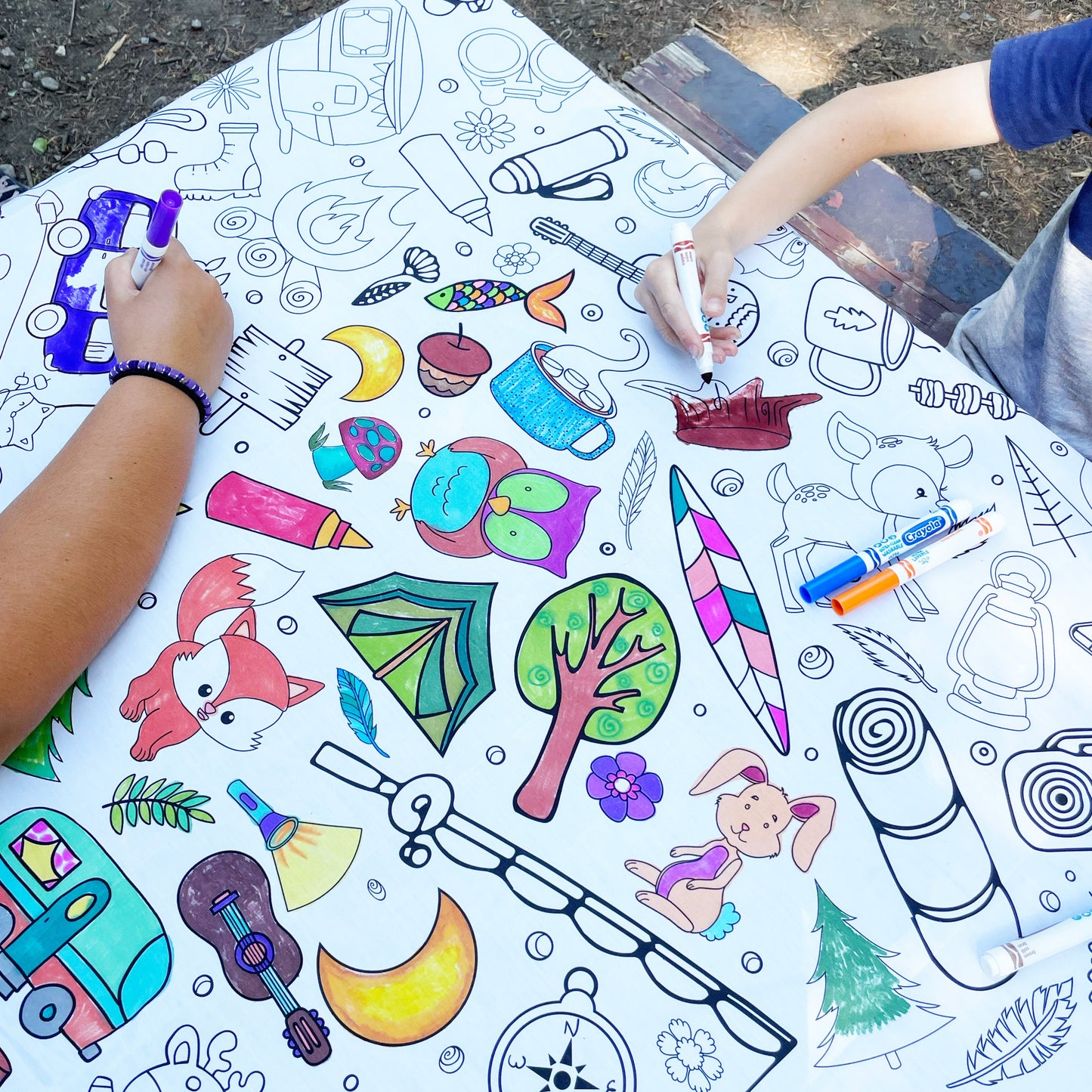 Coloring book with various illustrations on a large sheet of paper, with children's hands coloring.