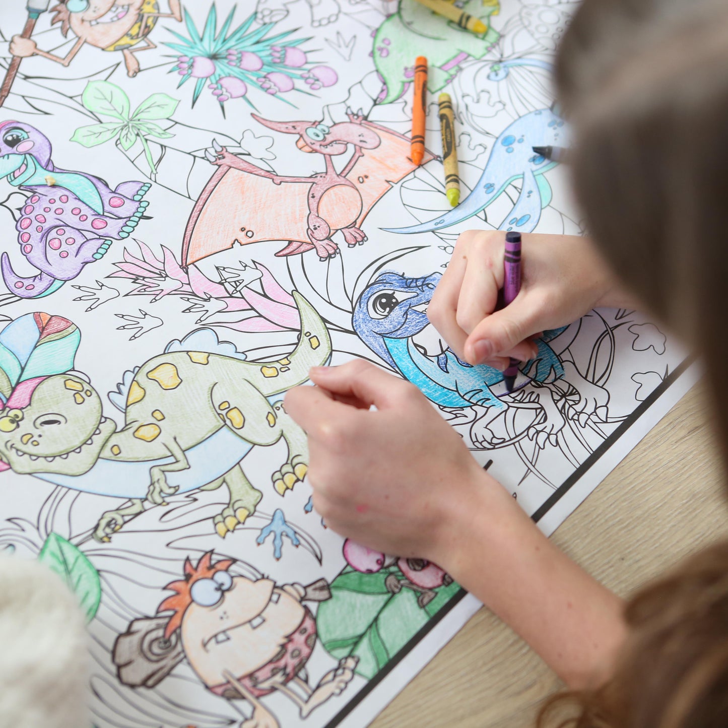 Person coloring a dinosaur-themed coloring sheet with crayons.