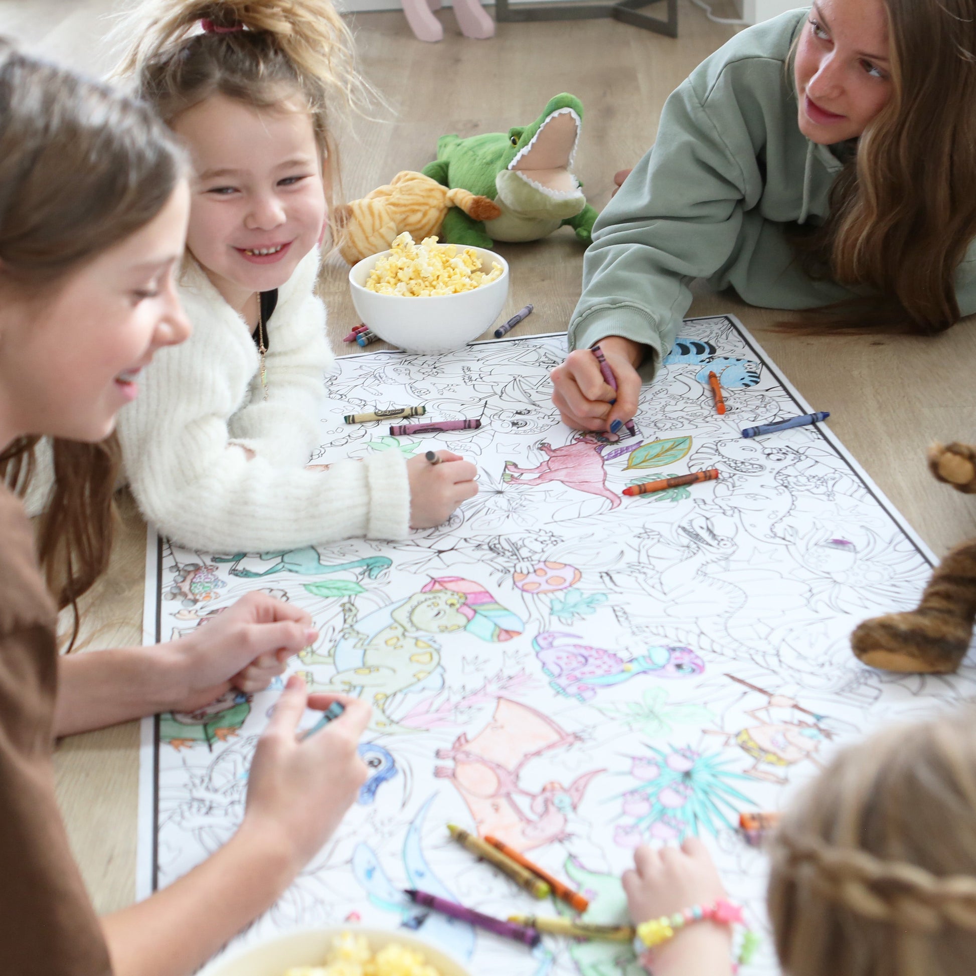 Children and a woman coloring on a large sheet of paper with crayons on the floor.