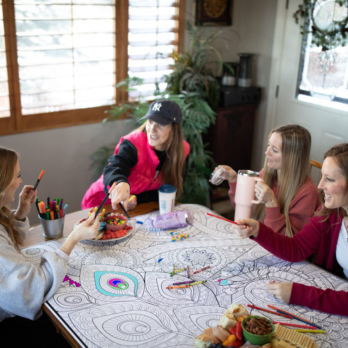 4 girls sitting around coloring a large poster and eating treats, laughing and pointing at eachother.