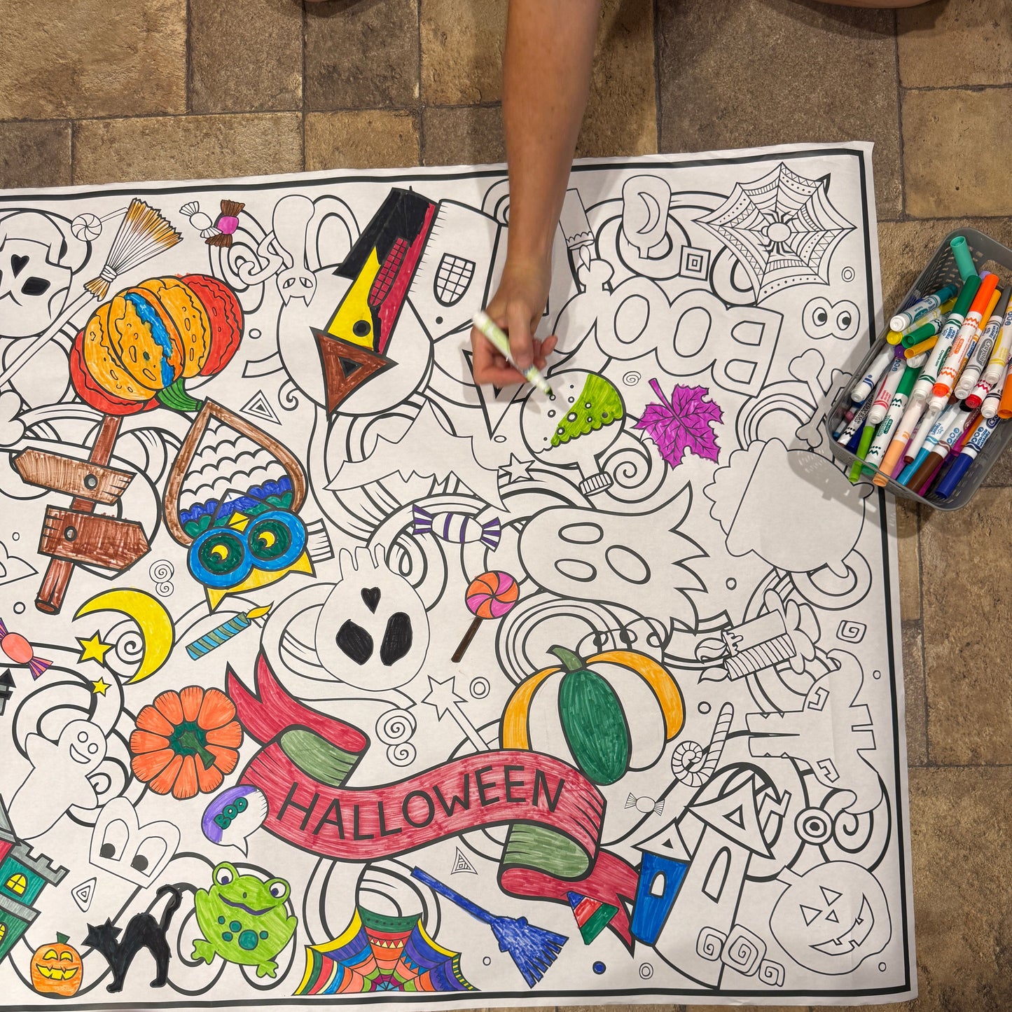 Coloring banner with Halloween-themed illustrations on the floor, with crayons on the side.