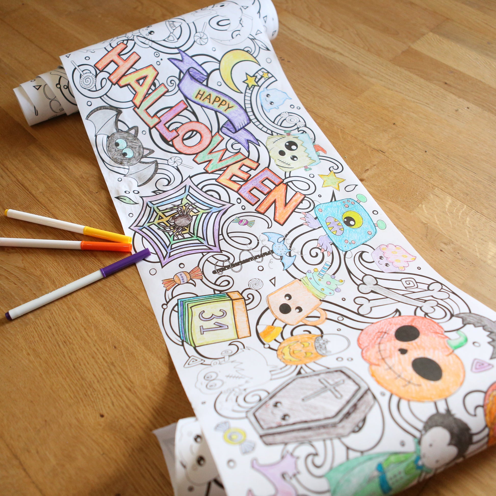 Long Coloring sheet with Halloween-themed illustrations and markers on a wooden floor