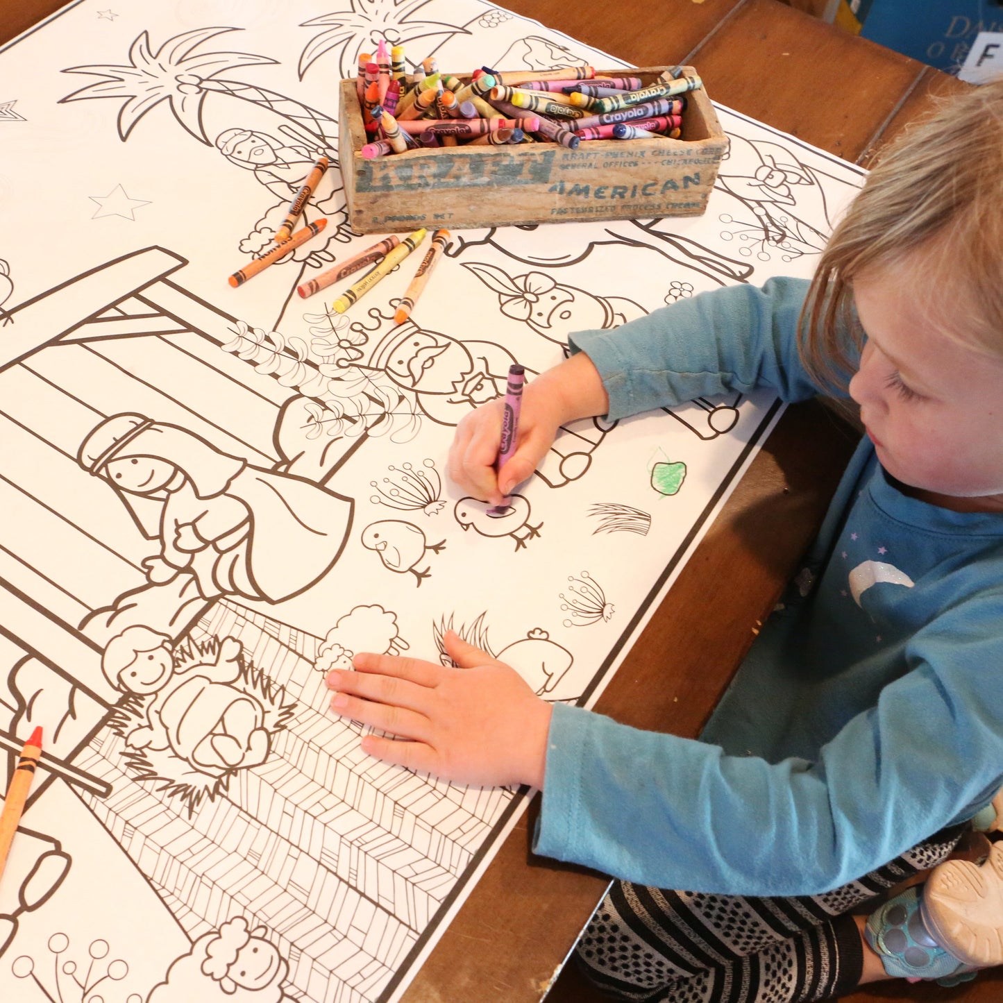 Child coloring a nativity coloring picture with crayons on a table