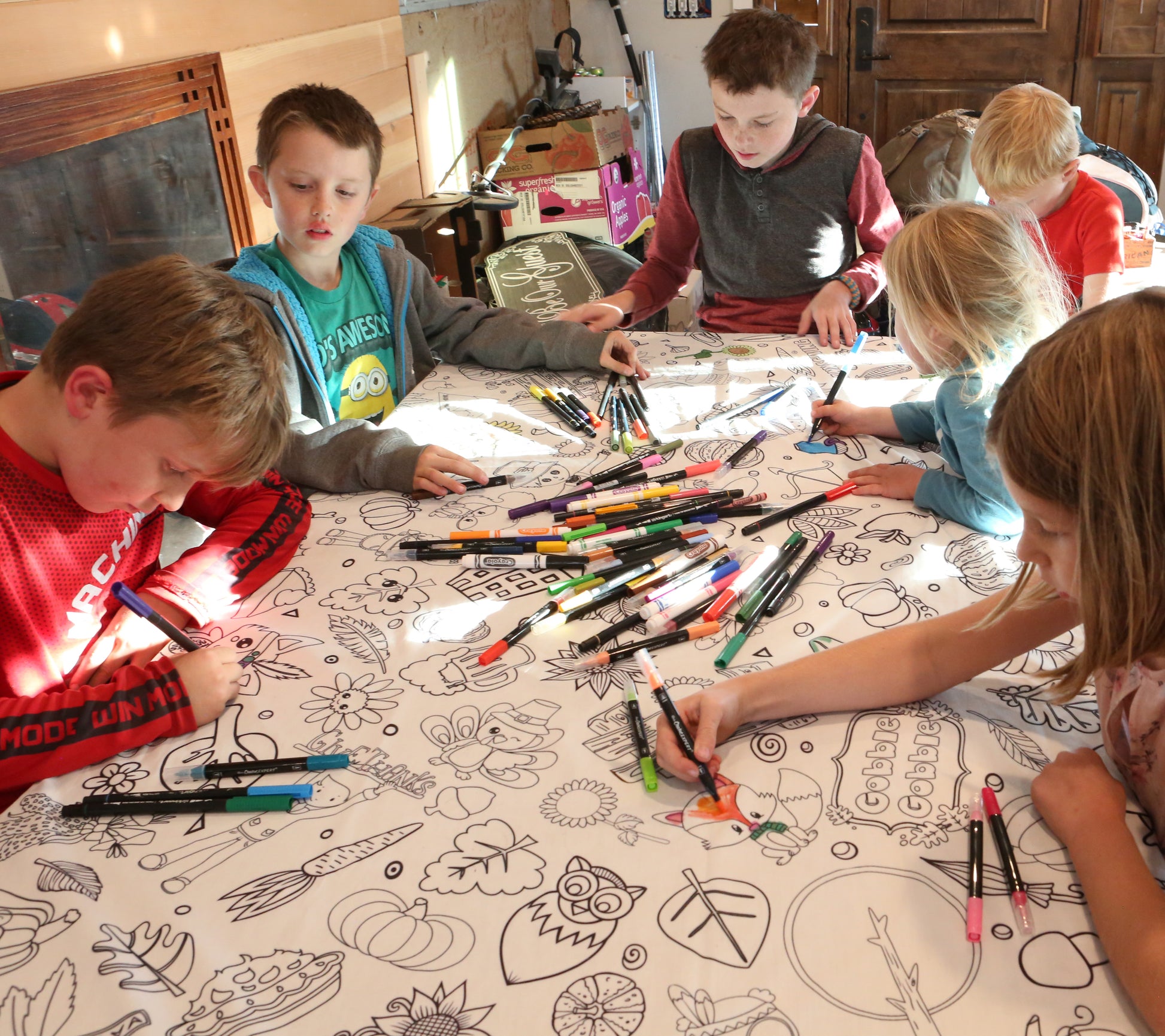 Children coloring at a thanksgiving 
table with markers on a patterned tablecloth.