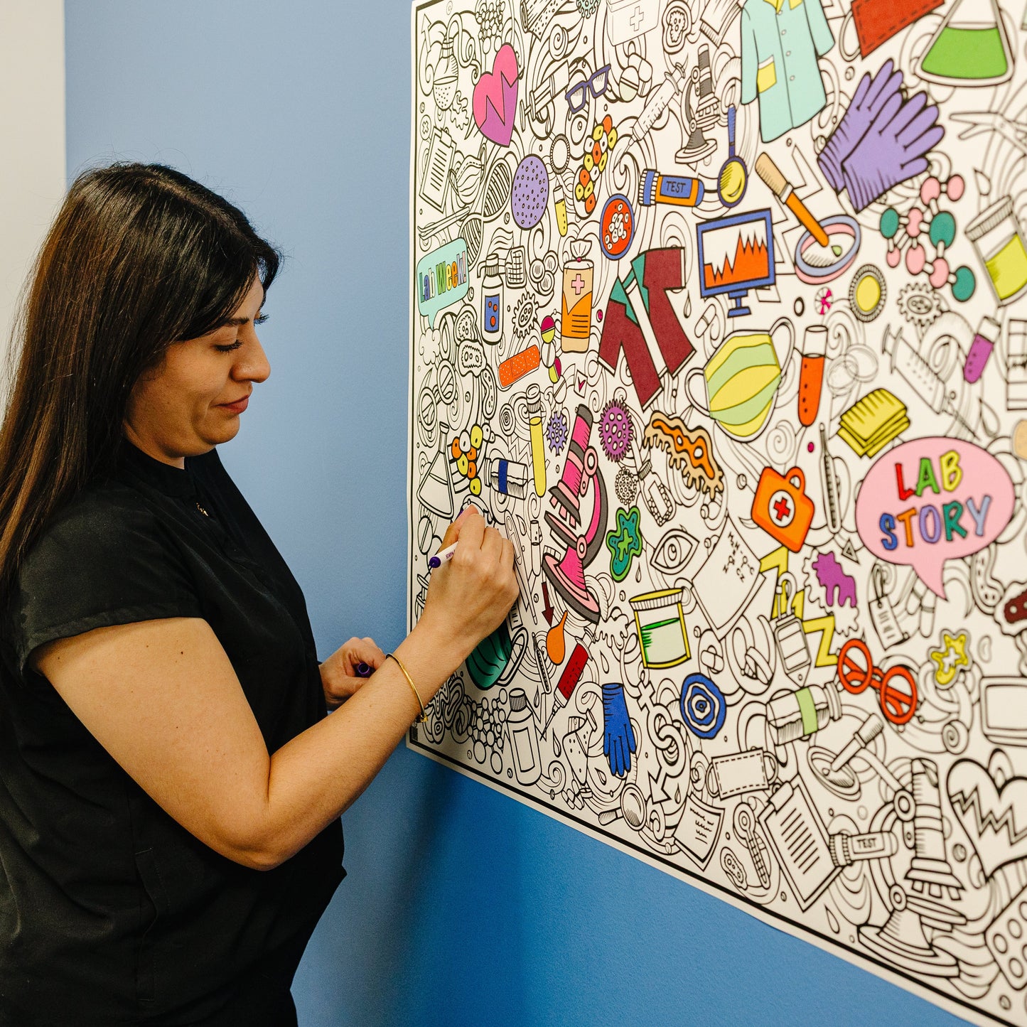 Person, likely a nurse, coloring a large, lab week collaborative wall coloring poster in a clinic setting.