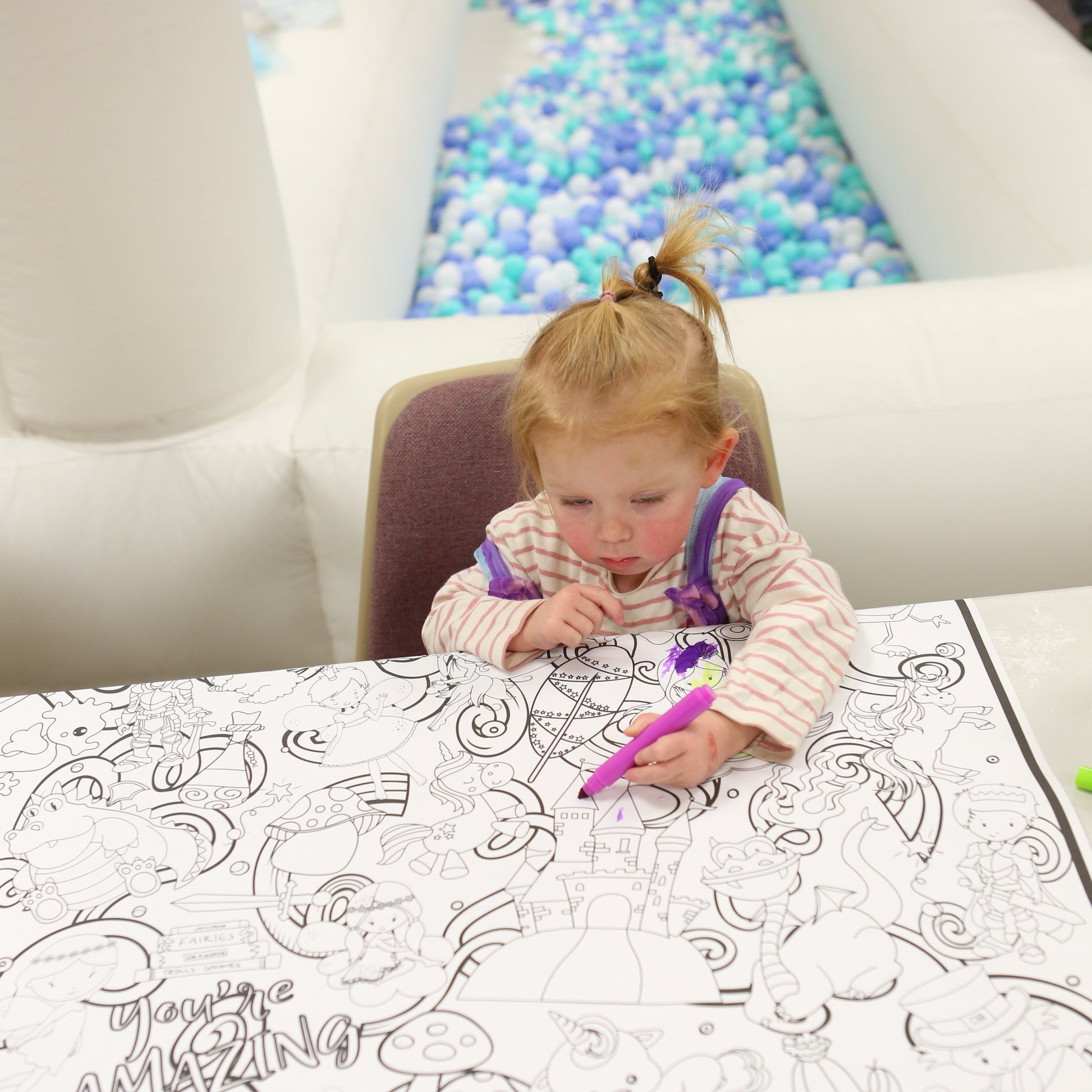 Child coloring on a large magical looking coloring sheet with a colorful ball pit in the background