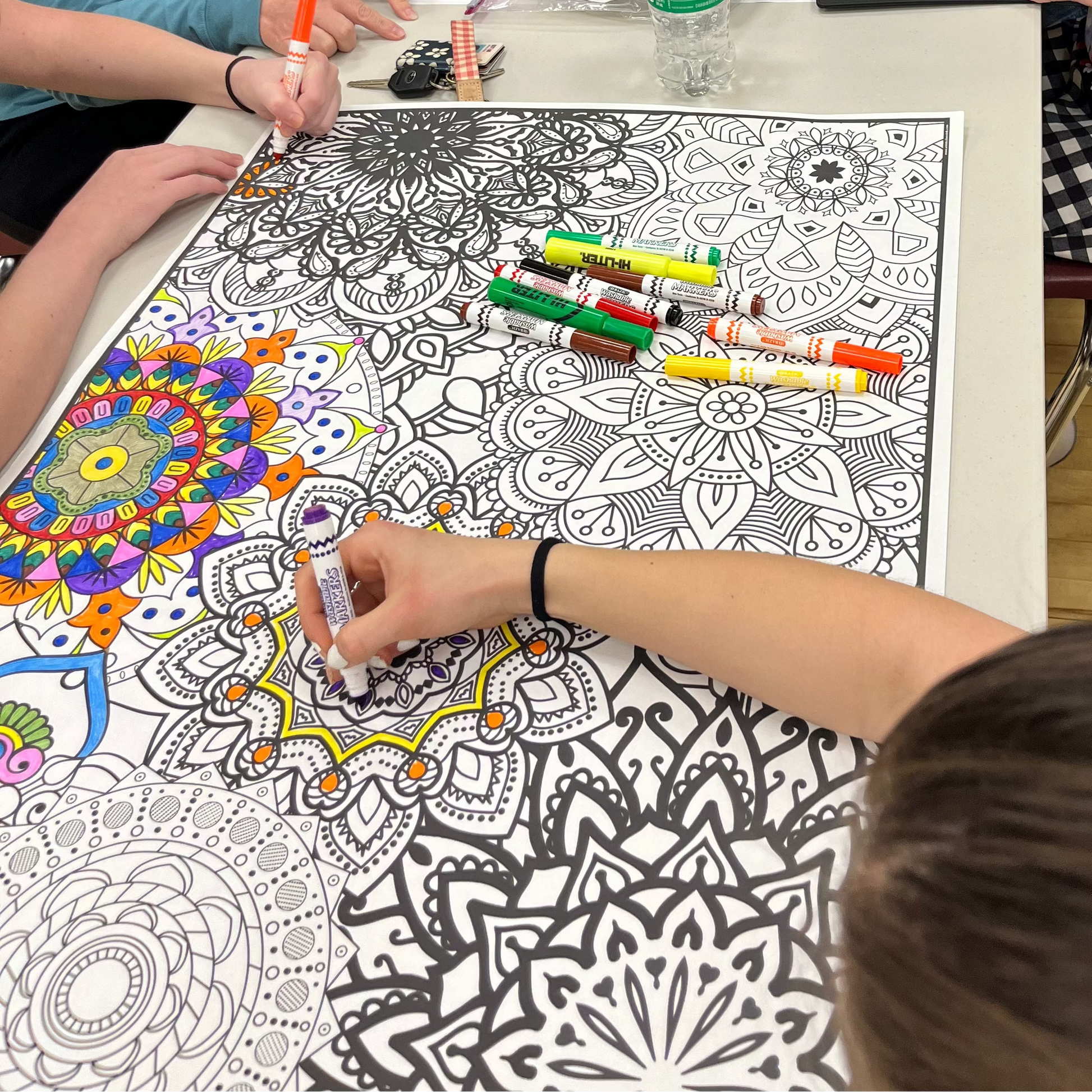 Group of people coloring intricate designs on large sheets at a table.