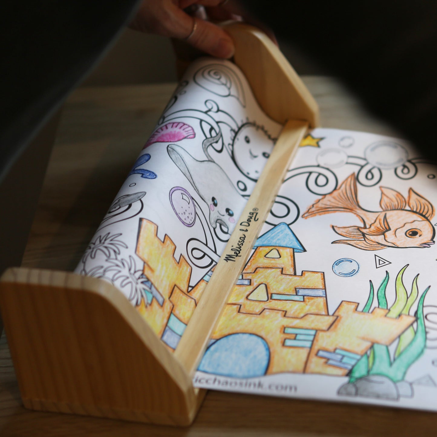 Coloring page with ocean-themed illustrations held open by a wooden holder.